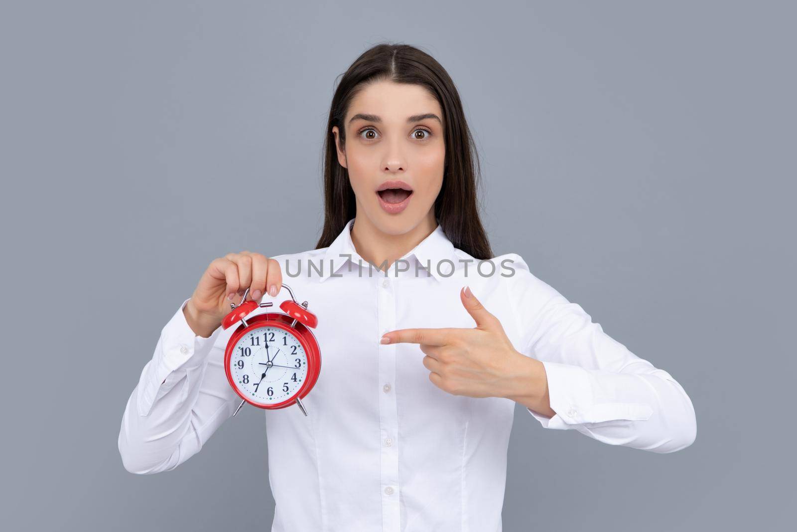 Surprised woman holding alarm watch. Isolated portrait. by RedFoxStudio