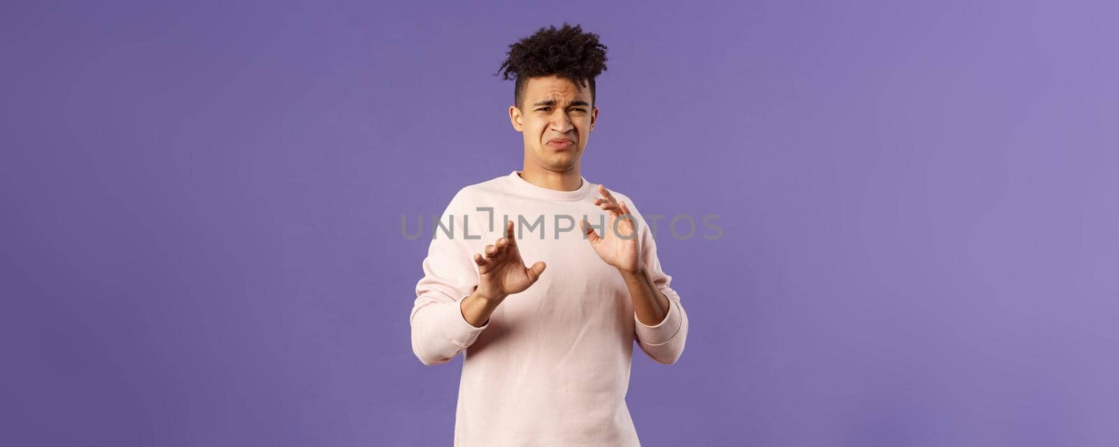 Phew get it away from me. Portrait of disgusted young man smelling something awful, step away and blocking it with raised arms, refuse grimacing with aversion and reluctance, purple background.