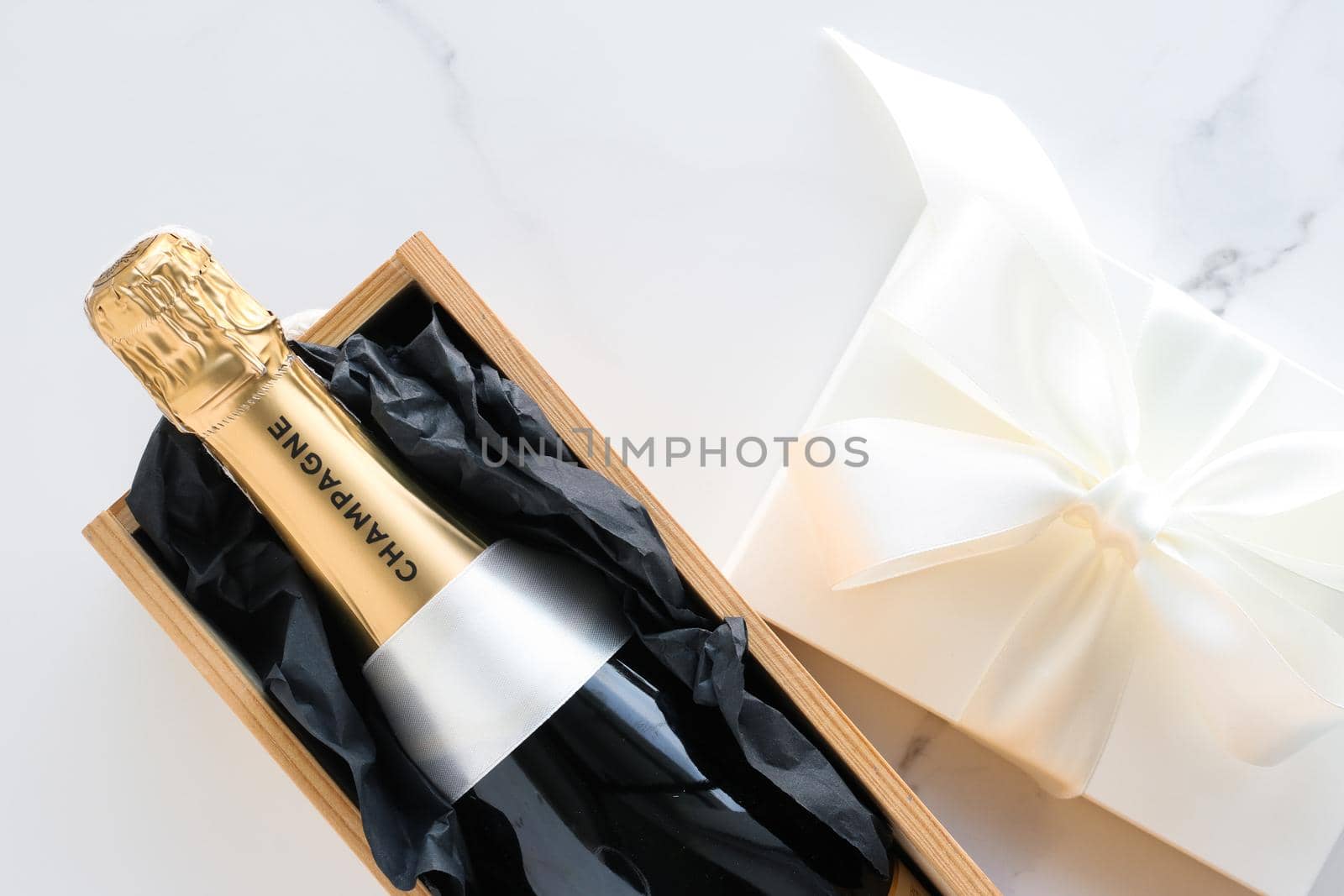 A champagne bottle and a gift box on marble by Anneleven