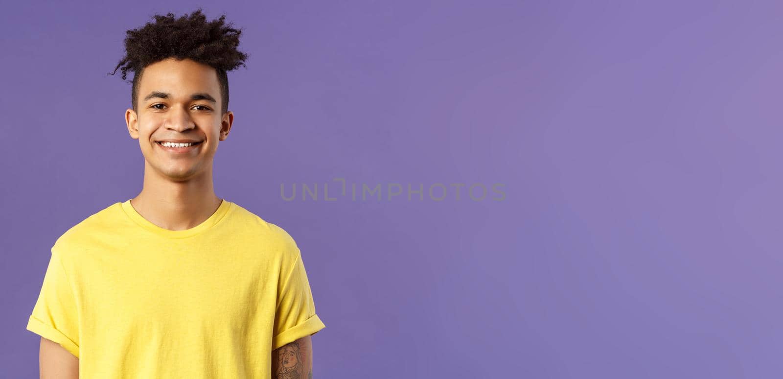 Close-up portrait of nice, friendly-looking hispanic male student in yellow t-shirt, grinning delighted, look upbeat happy and positive, standing enthusiastic with beaming smile purple background by Benzoix