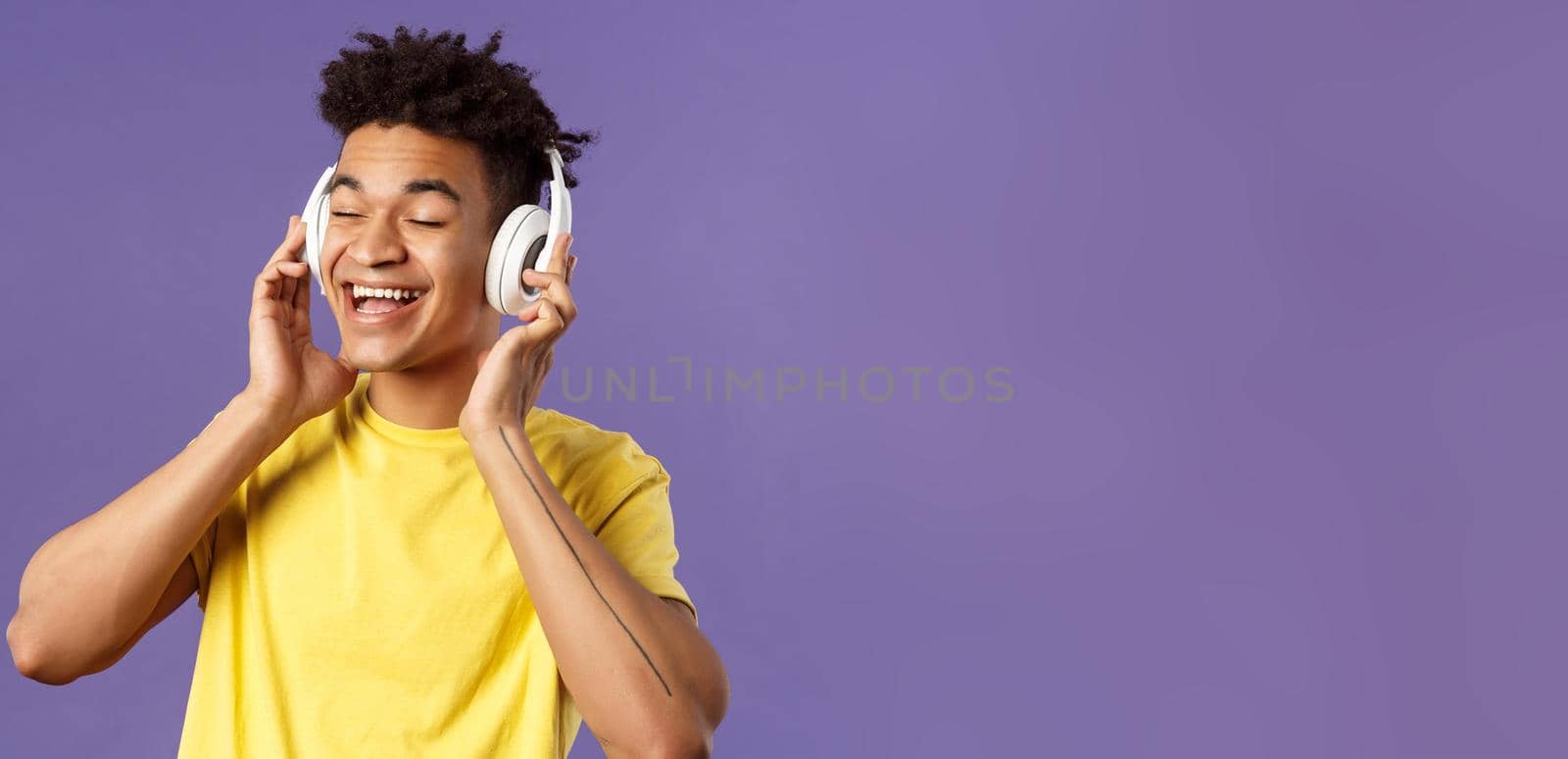 Close-up portrait of carefree, young upbeat man with dreads, close eyes and smiling pleased as listening to awesome new song favorite artist uploaded music platform, wear headphones by Benzoix