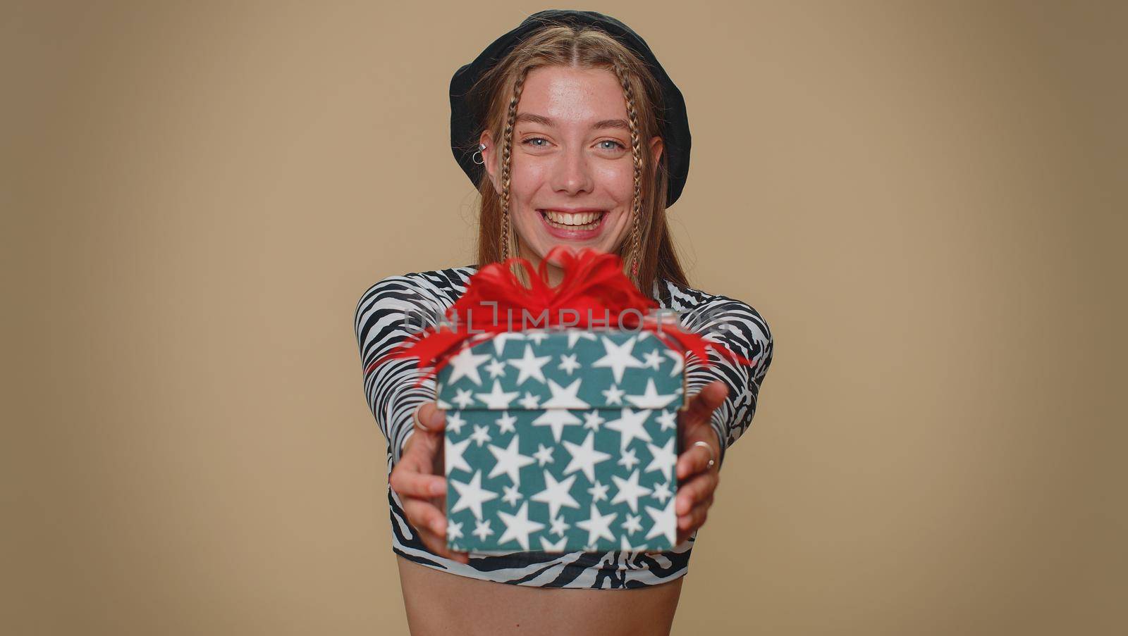 Positive smiling lovely pretty young woman presenting birthday gift box stretches out hands, offer wrapped present career bonus, celebrating party. Adult stylish girl on beige studio background indoor