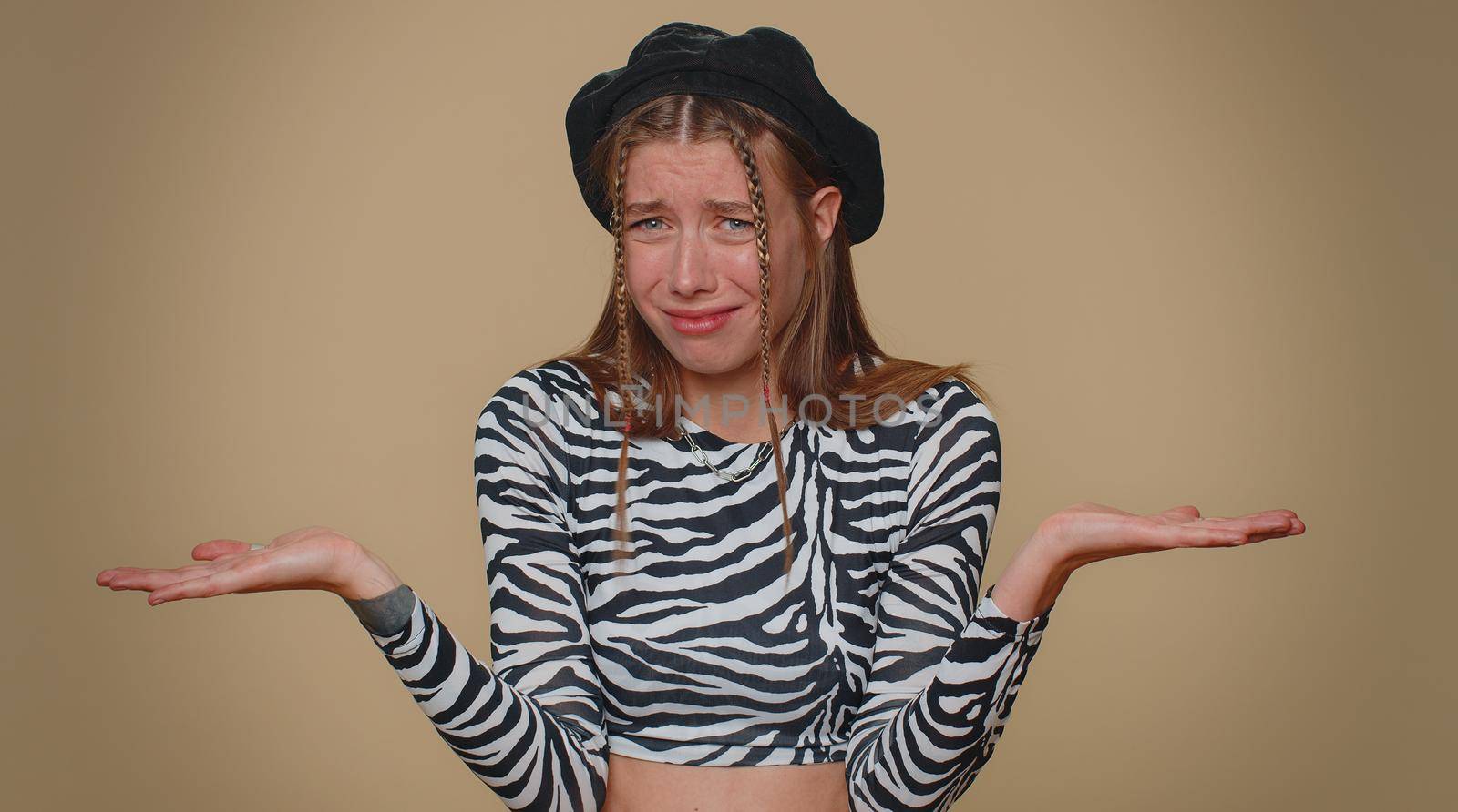 Pretty young woman raising hands in indignant expression, asking why, what reason of failure, demonstrating disbelief irritation by troubles. Adult stylish girl isolated on beige studio background