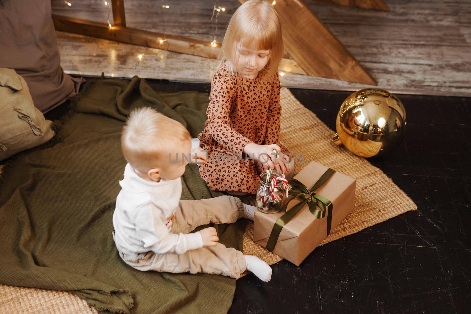 Little brother and sister play on Christmas eve in a beautiful house decorated for the New Year holidays. Children are playing with a Christmas gift. Scandinavian-style interior with live fir trees and a wooden staircase.