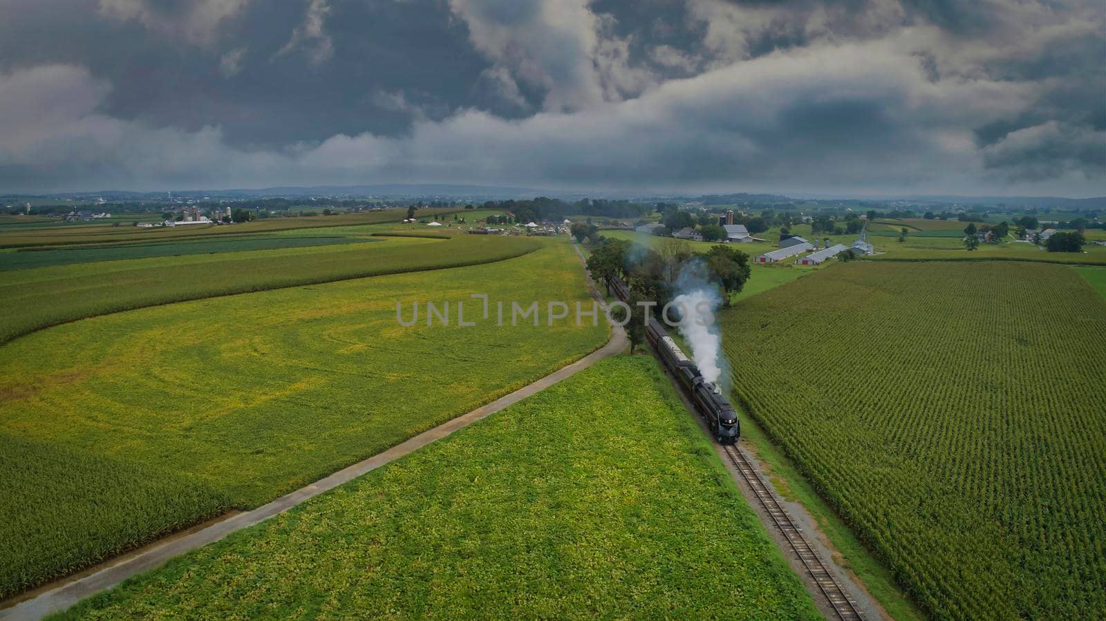 A Drone View of an Antique Steam Engine, Approaching, Blowing Steam and Traveling Along the Countryside on a Sunny Day