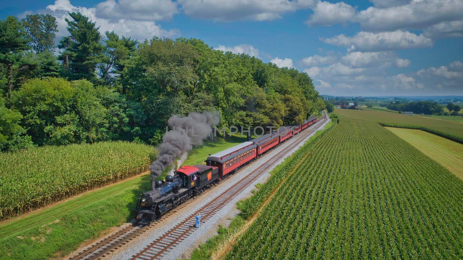 Ronks, Pennsylvania, August 29, 2021 - Drone View of an Antique Steam Engine, Approaching, Blowing Steam and Traveling Along the Countryside on a Sunny Day