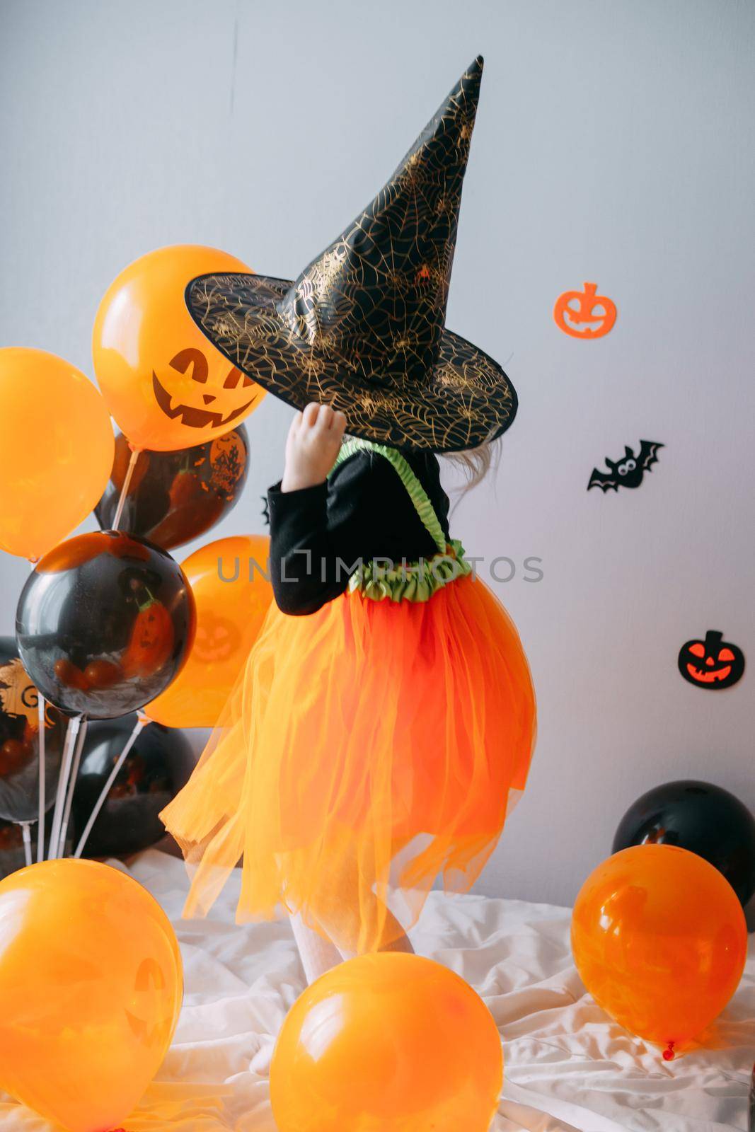 Children's Halloween - a girl in a witch hat and a carnival costume with airy orange and black balloons at home. Ready to celebrate Halloween by Annu1tochka