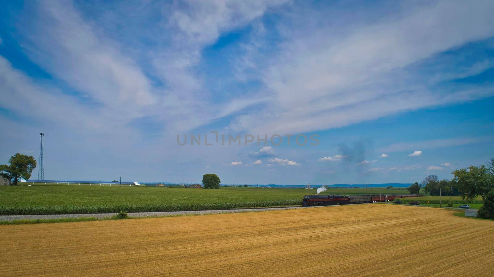 Aerial View of a Steam Passenger Train Approaching, Traveling Through Farmlands, With Corn and Wheat Fields, on a Beautiful Sunny Day.