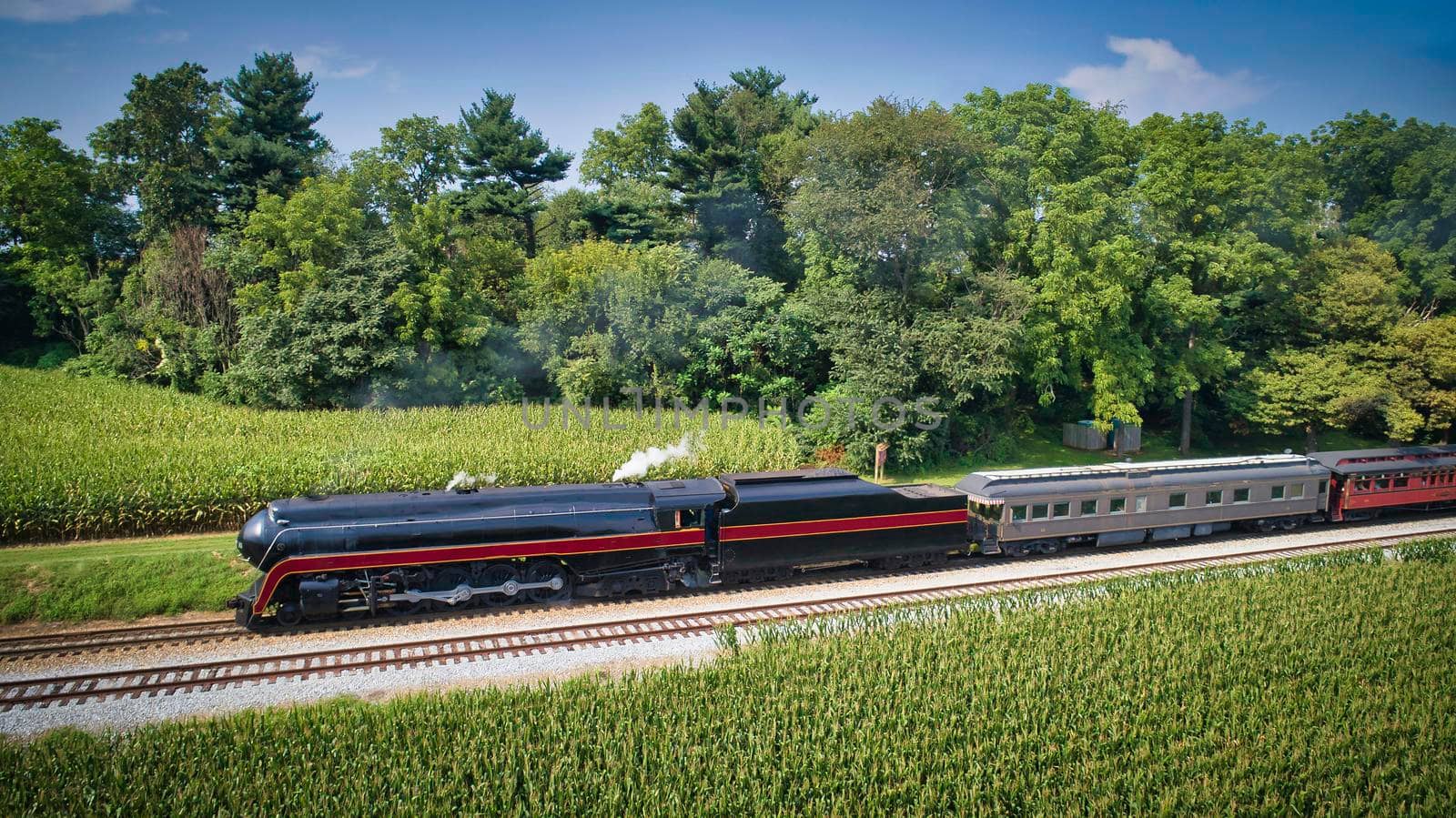 Drone View of an Antique Steam Engine, Approaching, Blowing Steam and Traveling Along the Countryside on a Sunny Day