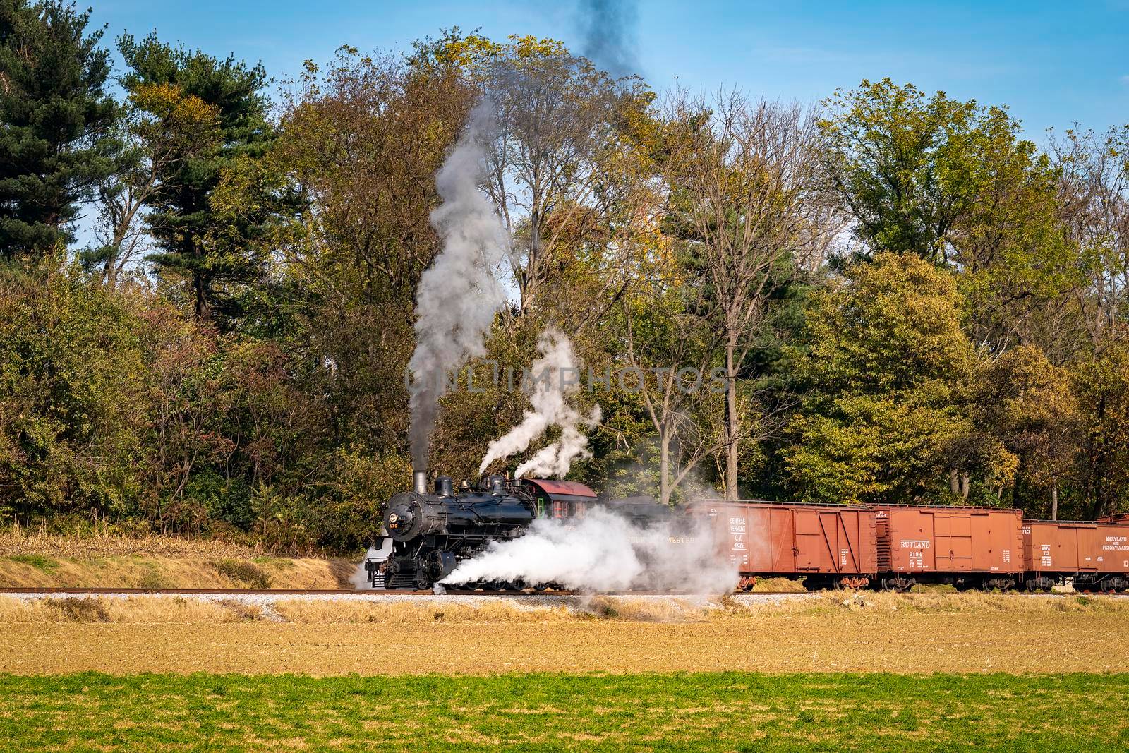 Ronks, Pennsylvania, November 8, 2021 - A View of a Restored Steam Freight Train Blowing Smoke and Steam Traveling Along a Rural Countryside on a Sunny Day