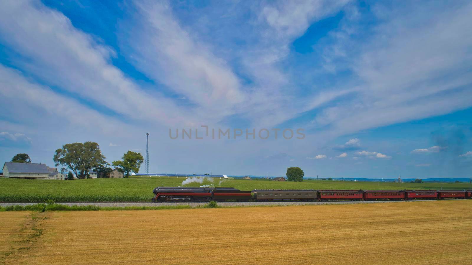Aerial View of a Steam Passenger Train Approaching, Traveling Through Farmlands, With Corn and Wheat Fields, on a Beautiful Sunny Day.