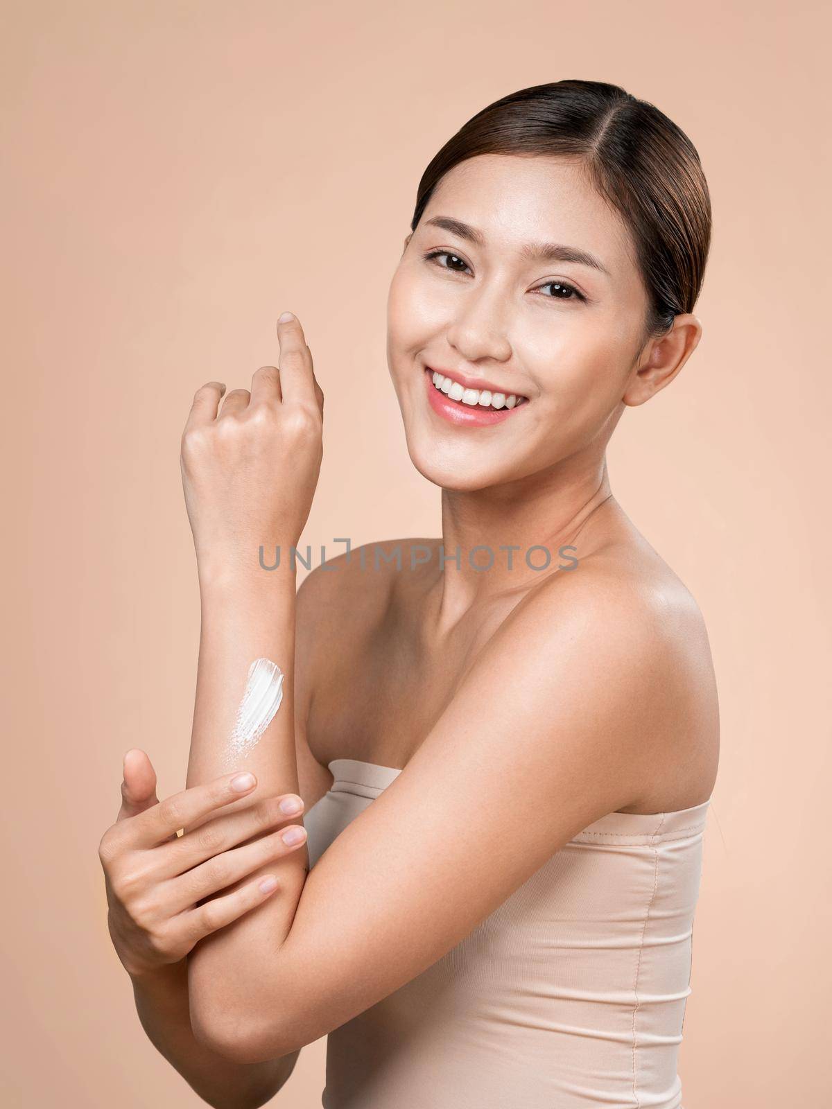 Ardent girl with soft makeup applying moisturizing skincare cream on her arm, isolated background. Skincare cream applied by female model concept.