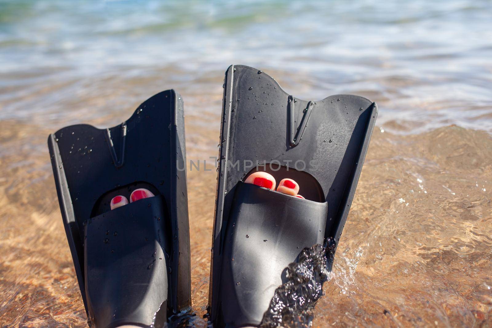 A woman in black flippers splashes near the shore. Fins stick out of the water. Swimming equipment. Summer holidays, fun, exploring the sea world concept. Space for copy.