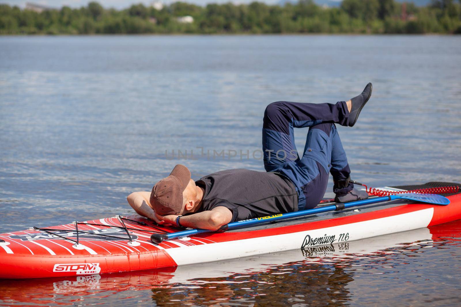 12.07.2022 Krasnoyarsk, Russia. SUP board Stand up paddle man boarding on lake standing happy on blue water. A man swims and rests on a SUP board on the river