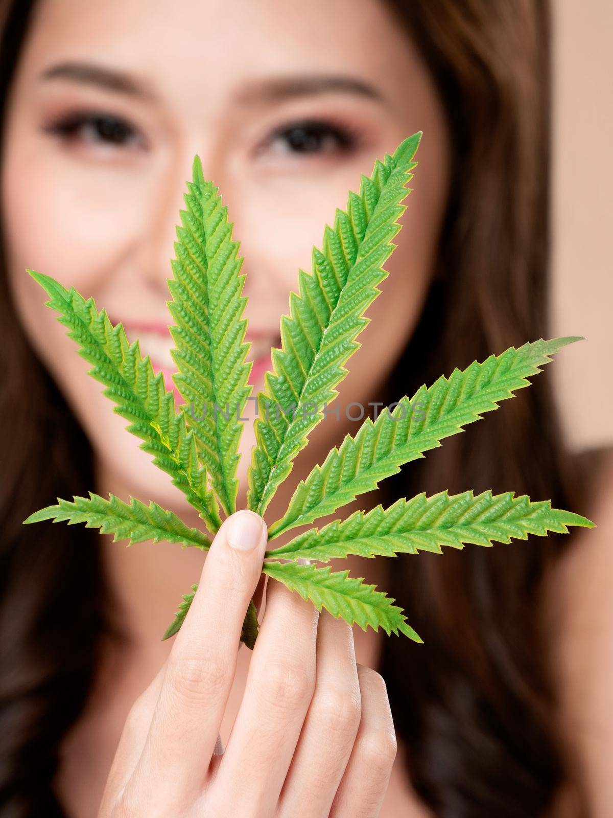 Closeup portrait of young ardent girl with healthy fresh skin holding green hemp leaf. Combination of beauty and cannabis concept.