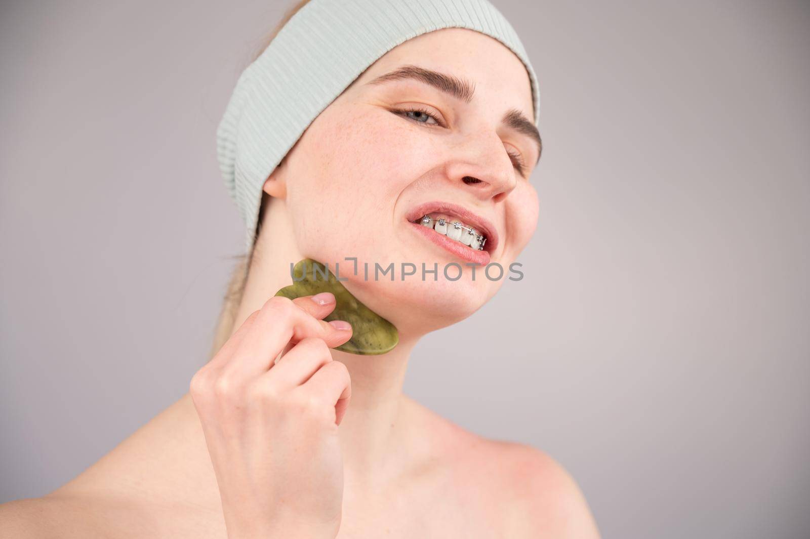 Portrait of a young woman massages her face with a gouache scraper on a white background