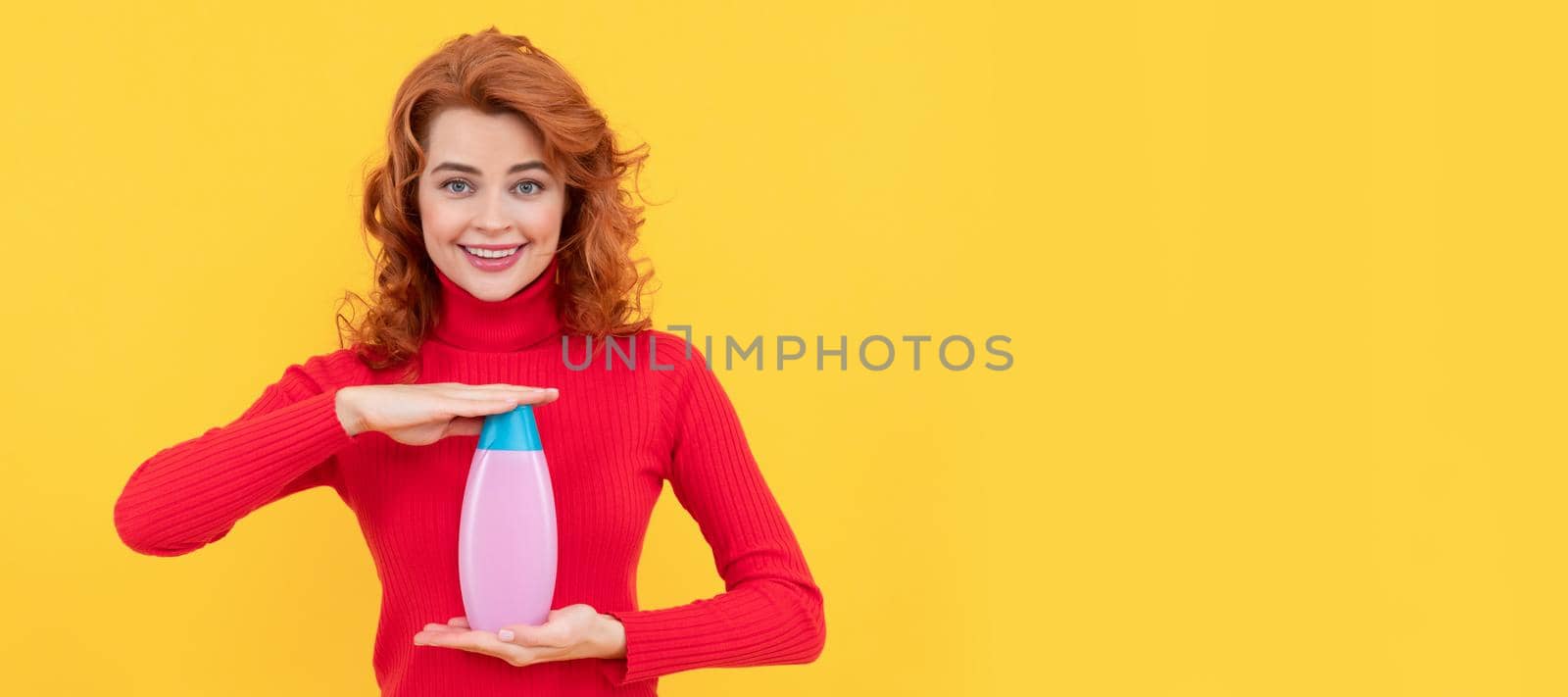 cheerful redhead woman curly dyed hair presenting body care product of shampoo, advertising.