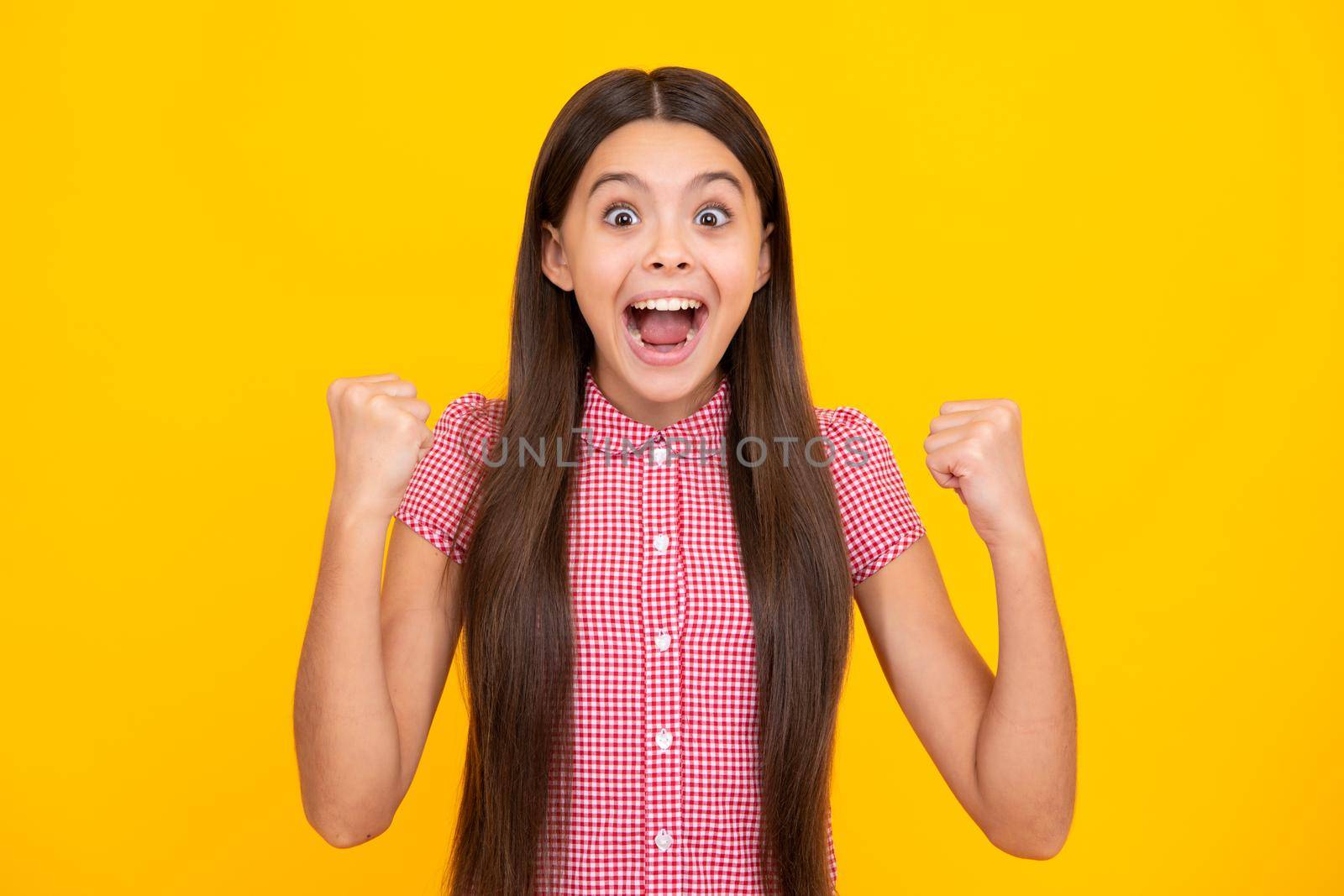 Amazed teen girl. Excited expression, cheerful and glad. Teenager child doing winner gesture celebrate clenching, say yes isolated on yellow background, studio portrait