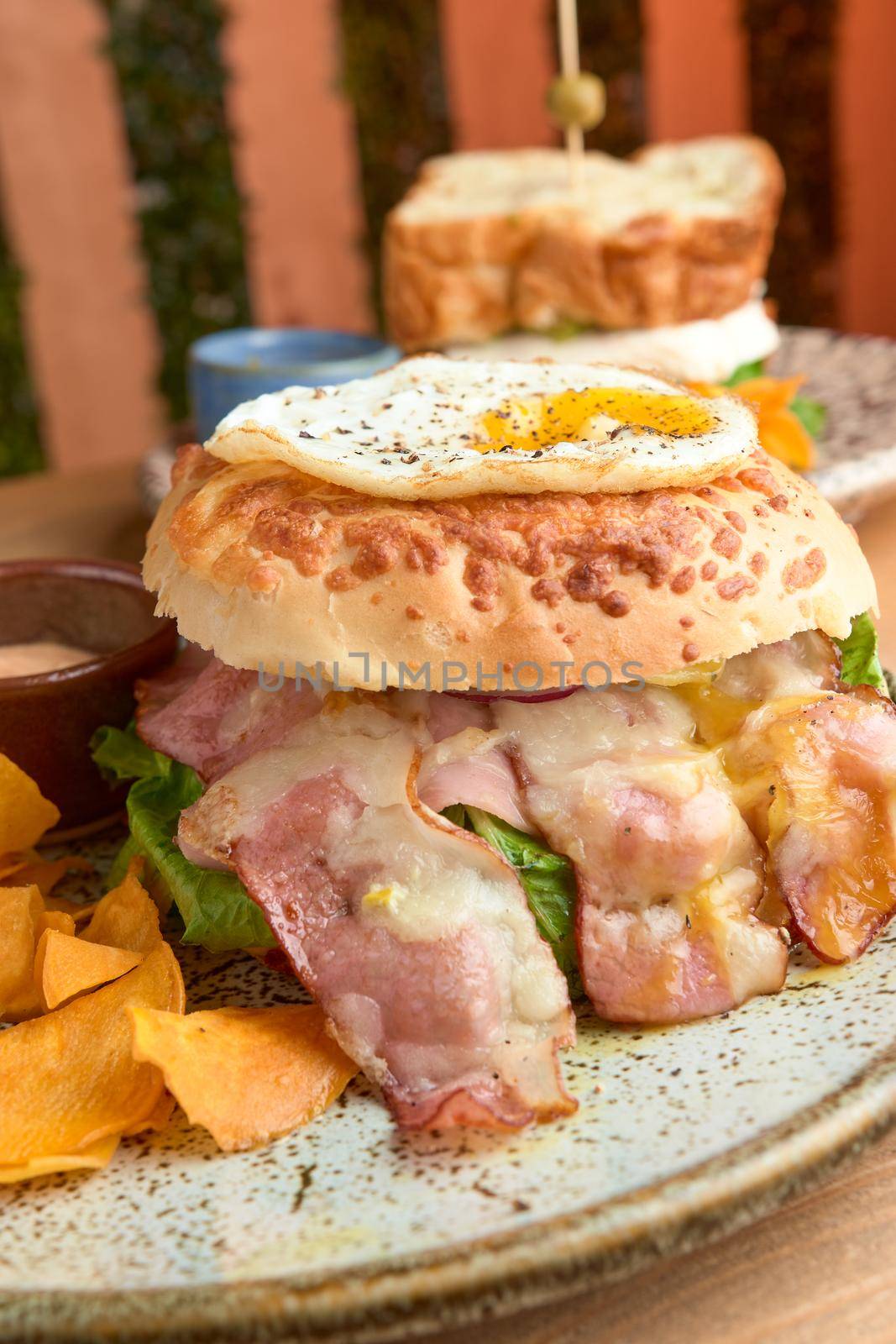 photo of delicious bacon burger accompanied with an egg, chipotle dressing and dehydrated bananas on wooden table. big hamburguer. accompanied with a panela sandwich