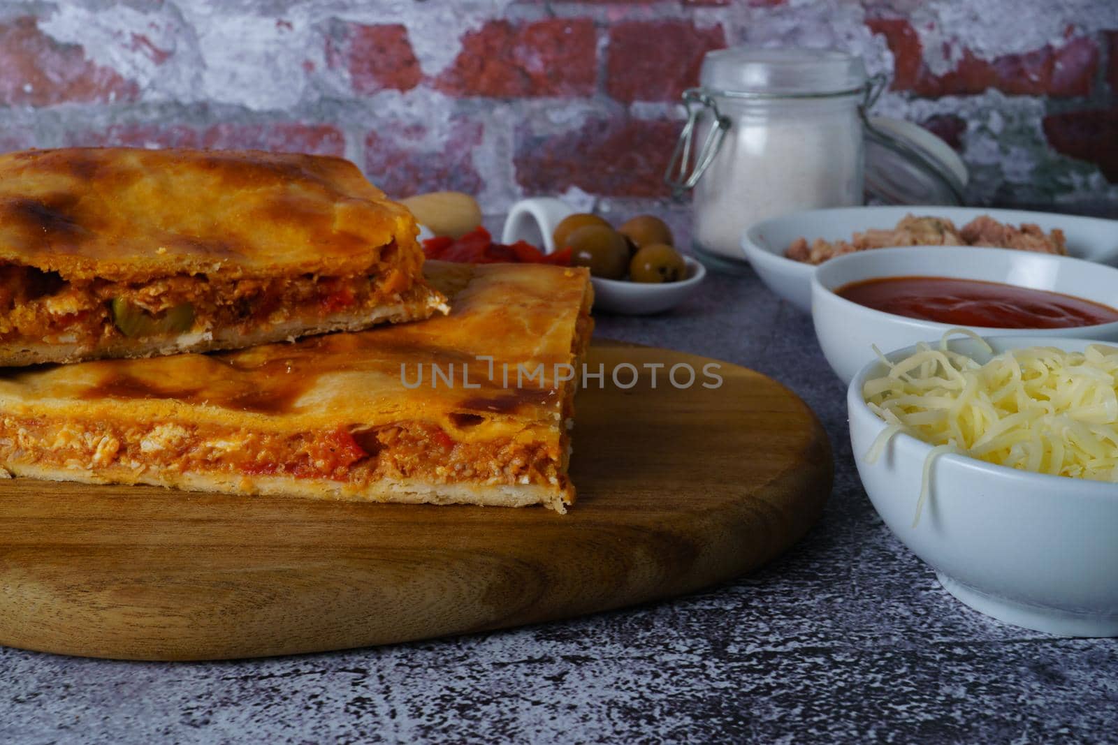 close-up of the filling of a tuna empanada with its ingredients on a wooden board with a brick background