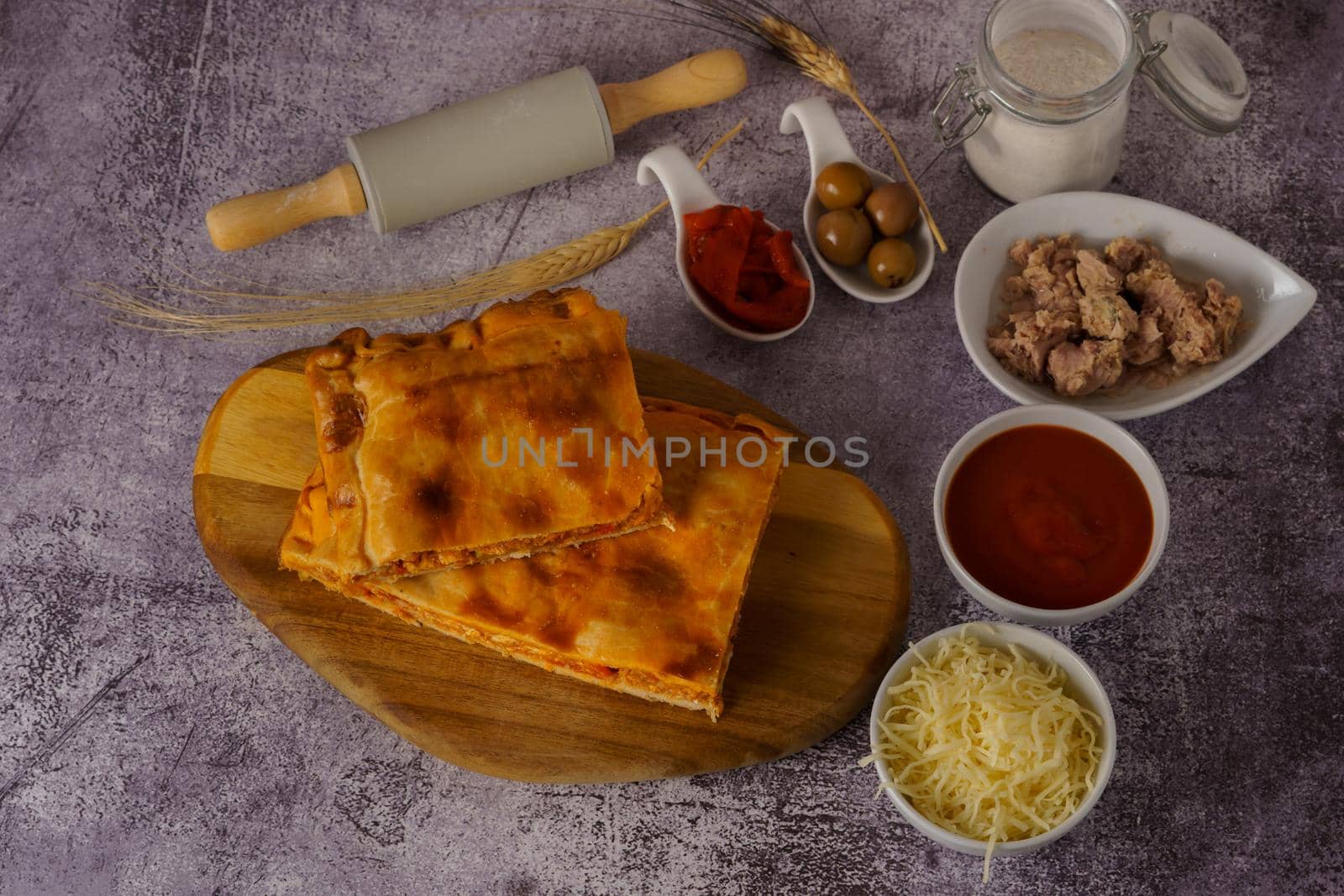 tuna empanada with all the ingredients separated in ceramic containers in the bottom of a red brick wall