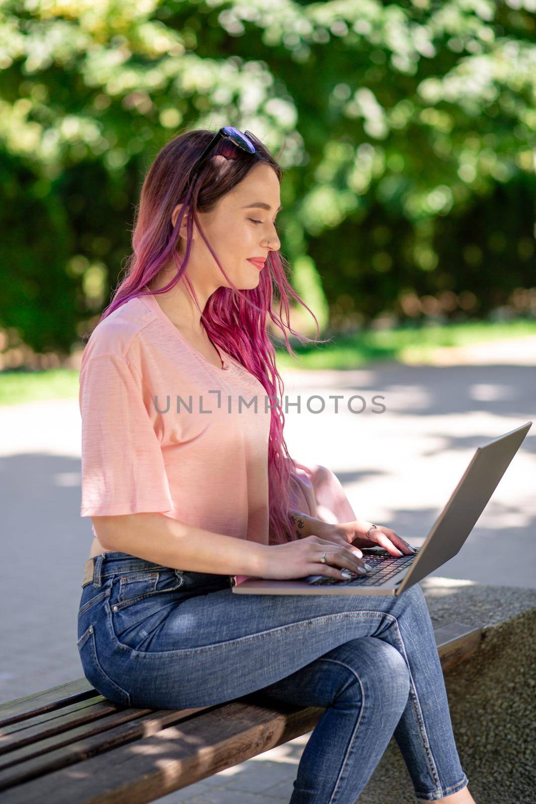 Young girl is studying in the spring park, sitting on the wooden bench and browsing on her laptop by nazarovsergey