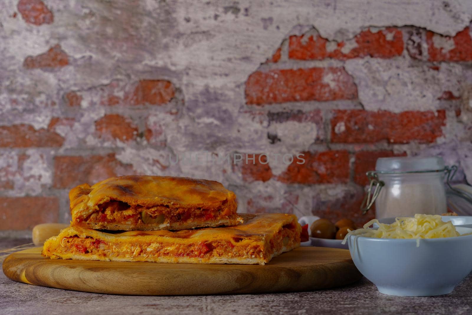 close-up of the filling of a tuna empanada with its ingredients on a wooden board with a brick background