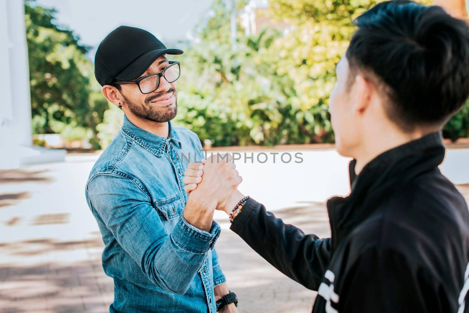 Two happy friends shaking hands in the street. Two people shaking hands on the street. Two smiling friends greet each other on the street by isaiphoto
