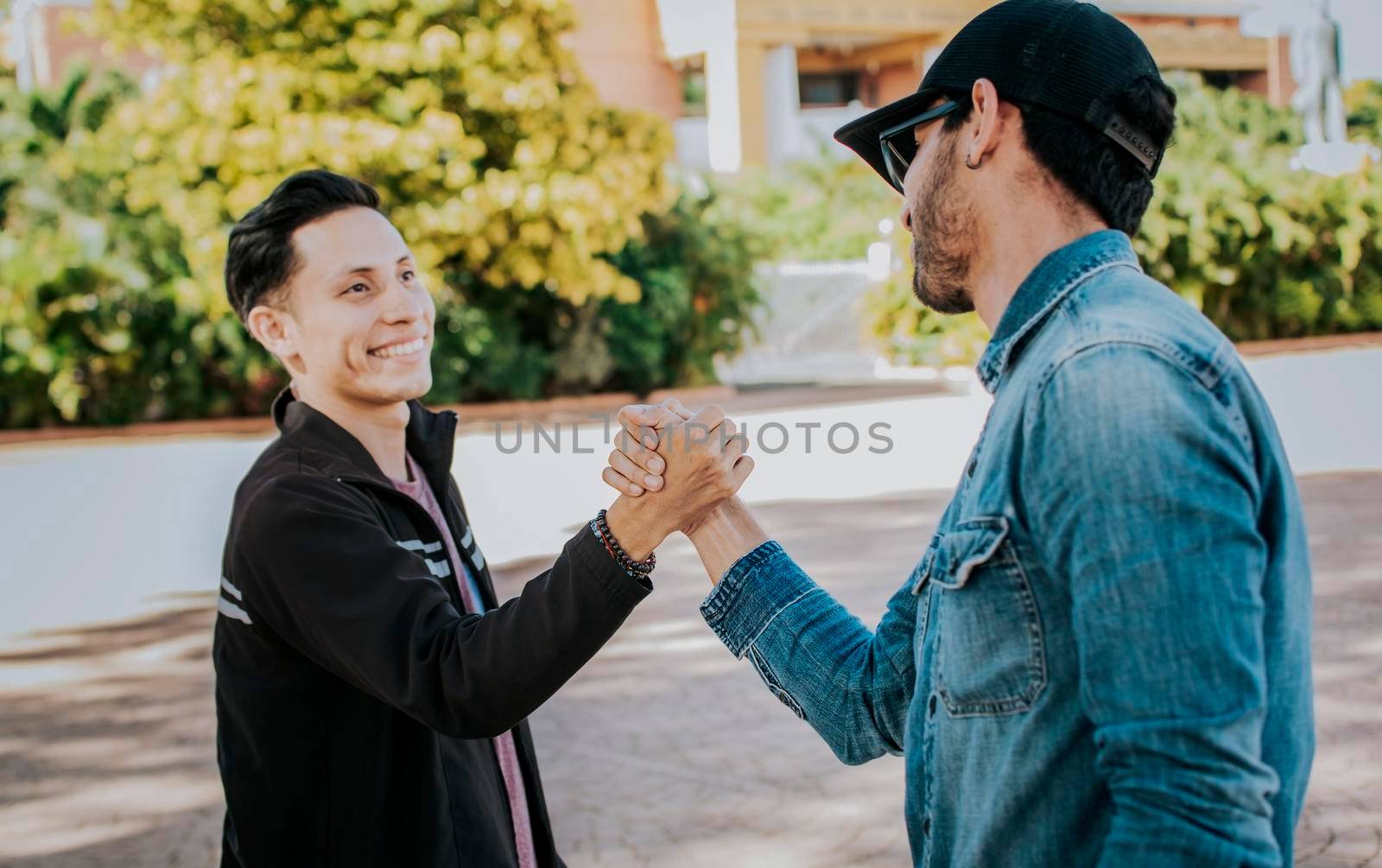 Two people shaking hands on the street. Two teenage friends shaking hands at each other outdoors. Concept of two friends greeting each other with handshake on the street. by isaiphoto