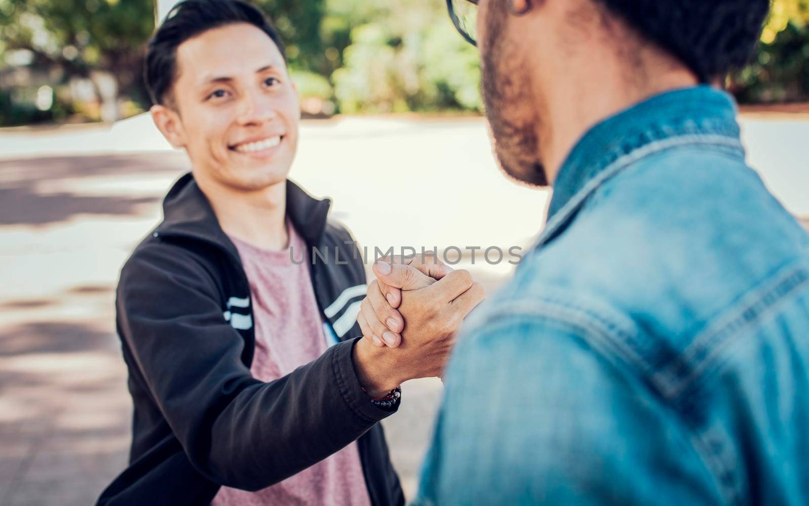 Two teenage friends shaking hands at each other outdoors. Two people shaking hands on the street. Concept of two friends greeting each other with handshake on the street by isaiphoto