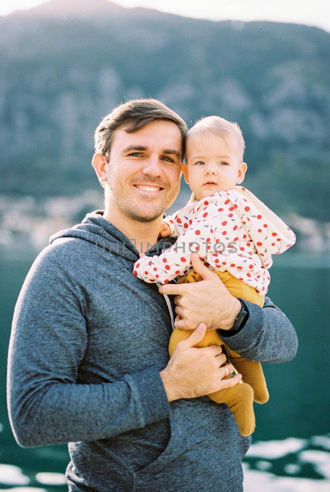 Smiling dad with a baby in his arms on the background of mountains. Portrait. High quality photo