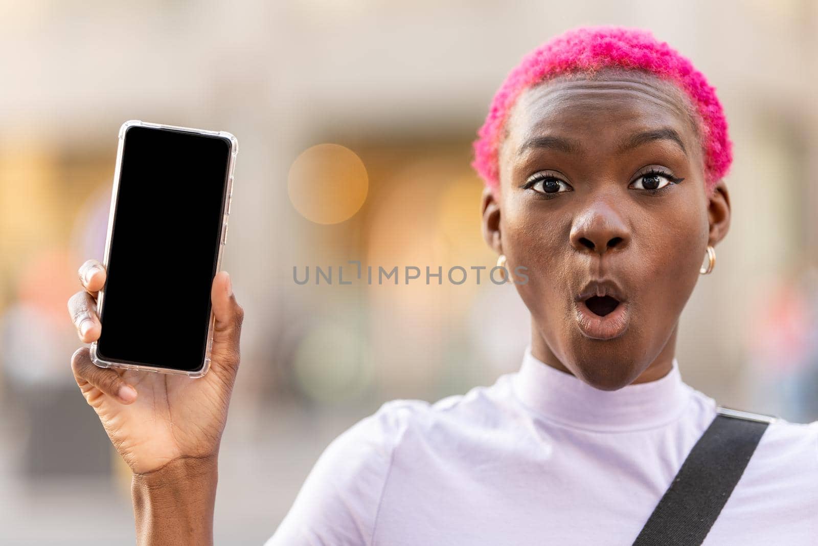 Stylish african woman with a surprised face showing a mobile phone screen outdoors