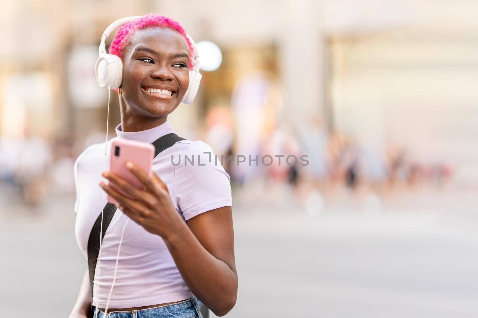 Smiling stylish afro woman smiling while listening music with the mobile in the street