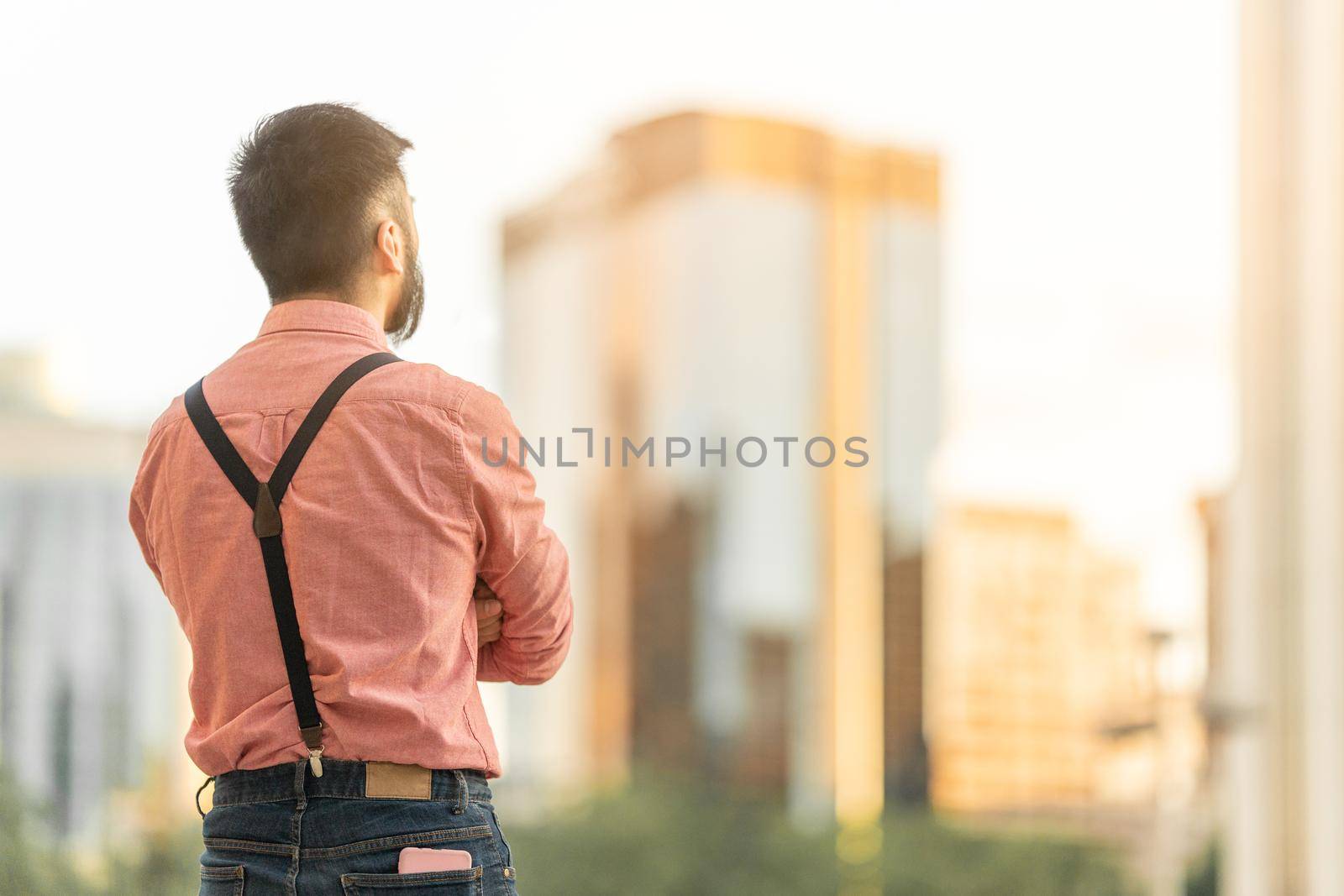 Back of an asian man in casual clothes looking the city landscape with skyscrapers at sunset