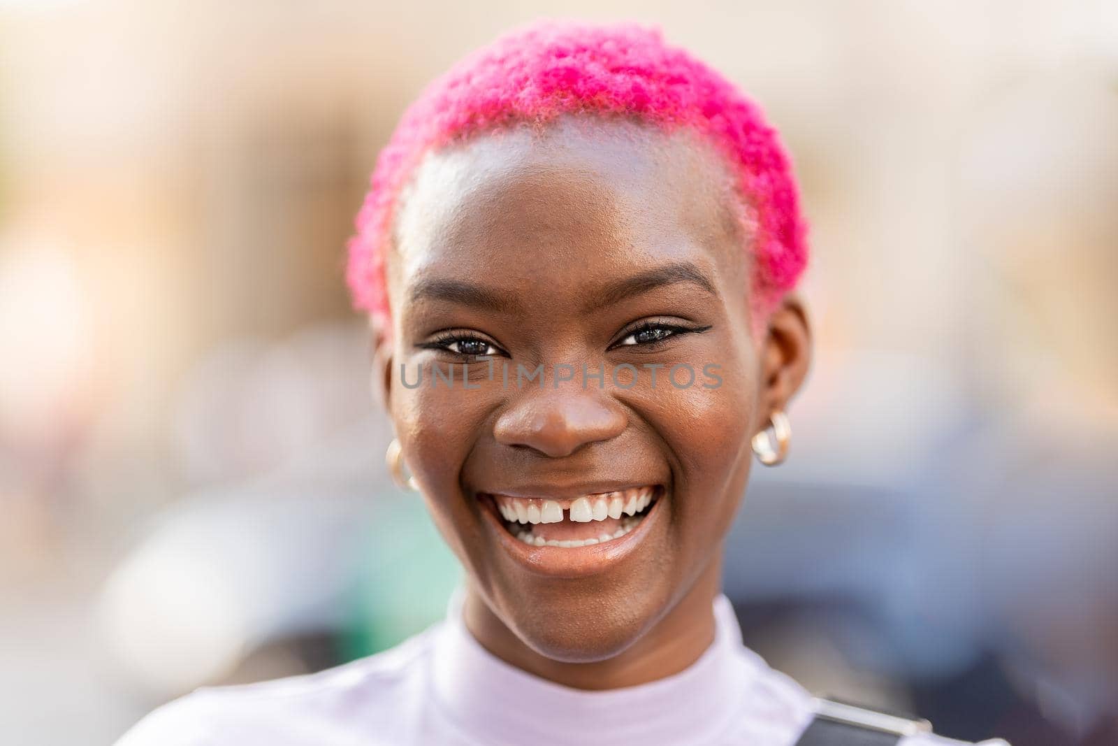 Portrait of a young african woman with short pink hair smiling to the camera in the street