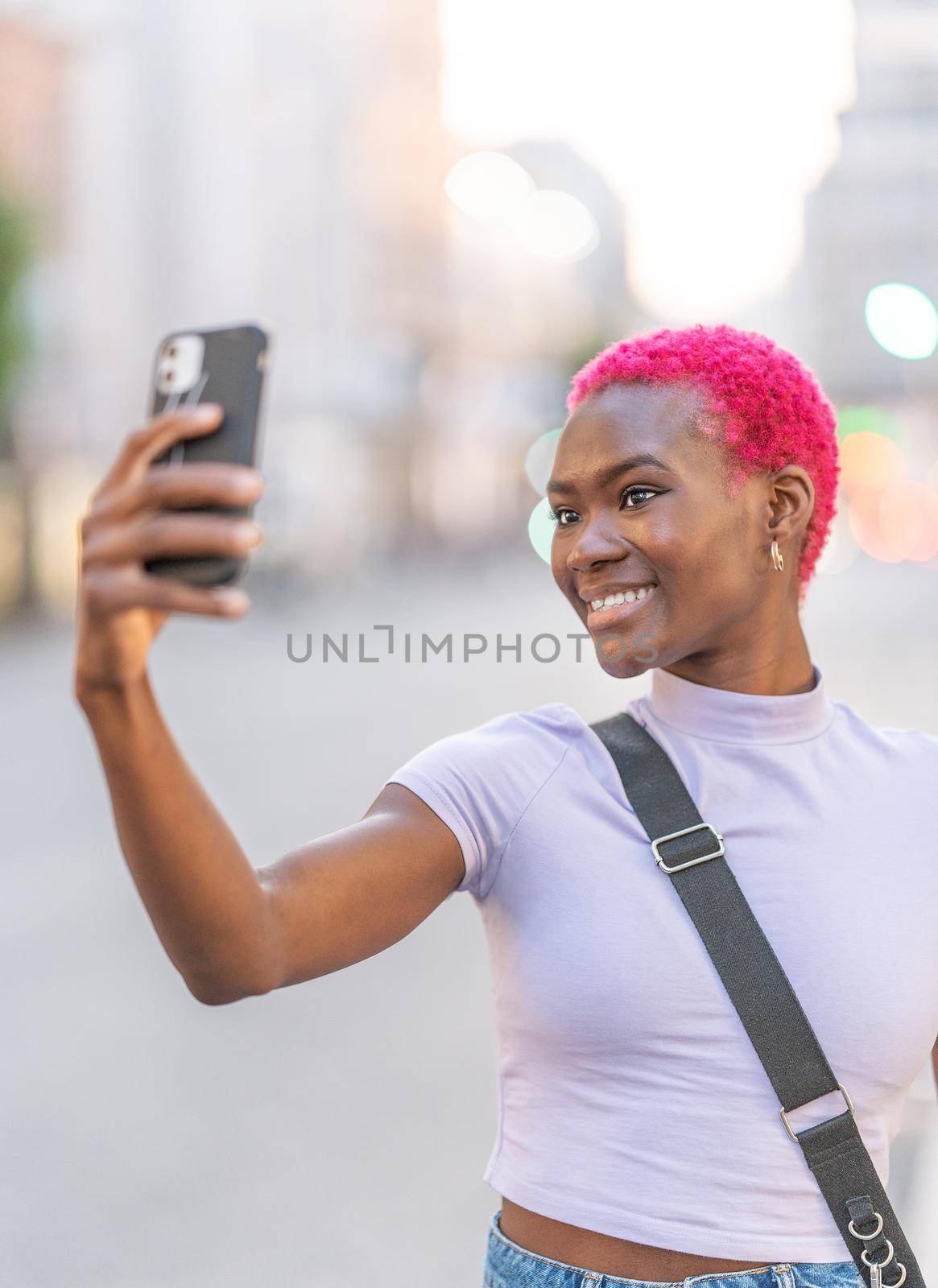 Vertical portrait of a stylish afro woman with short hair taking a selfie with a mobile in a city
