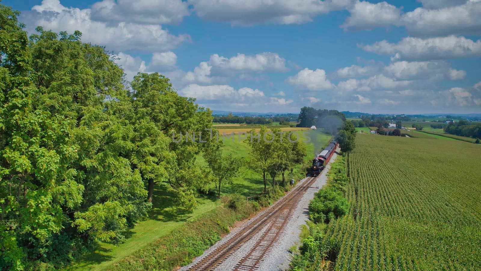 Drone View of an Antique Steam Engine, Approaching, Blowing Steam and Traveling Along the Countryside on a Sunny Day