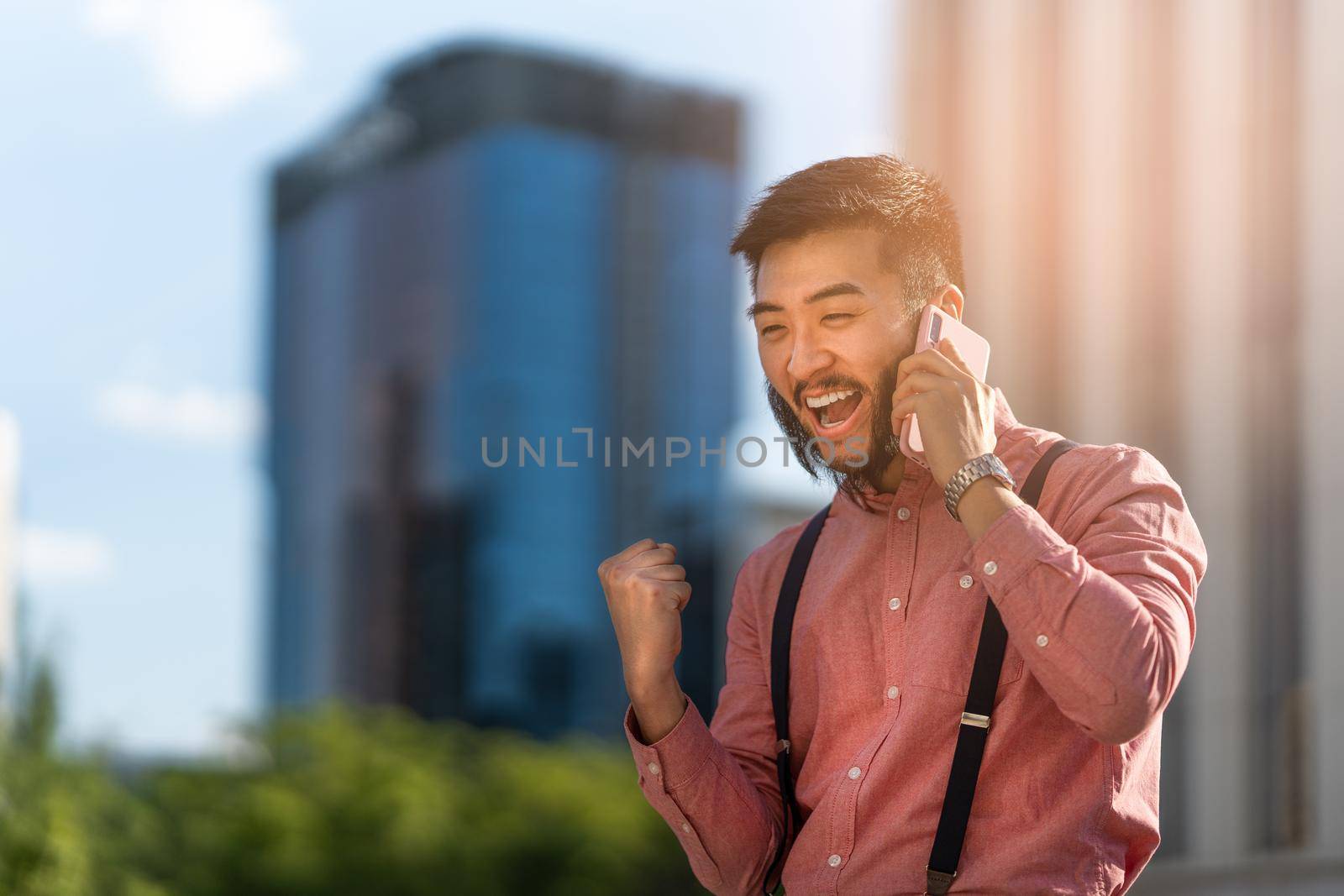 Asian businessman gesturing success while talking on the phone with a cityscape in the background