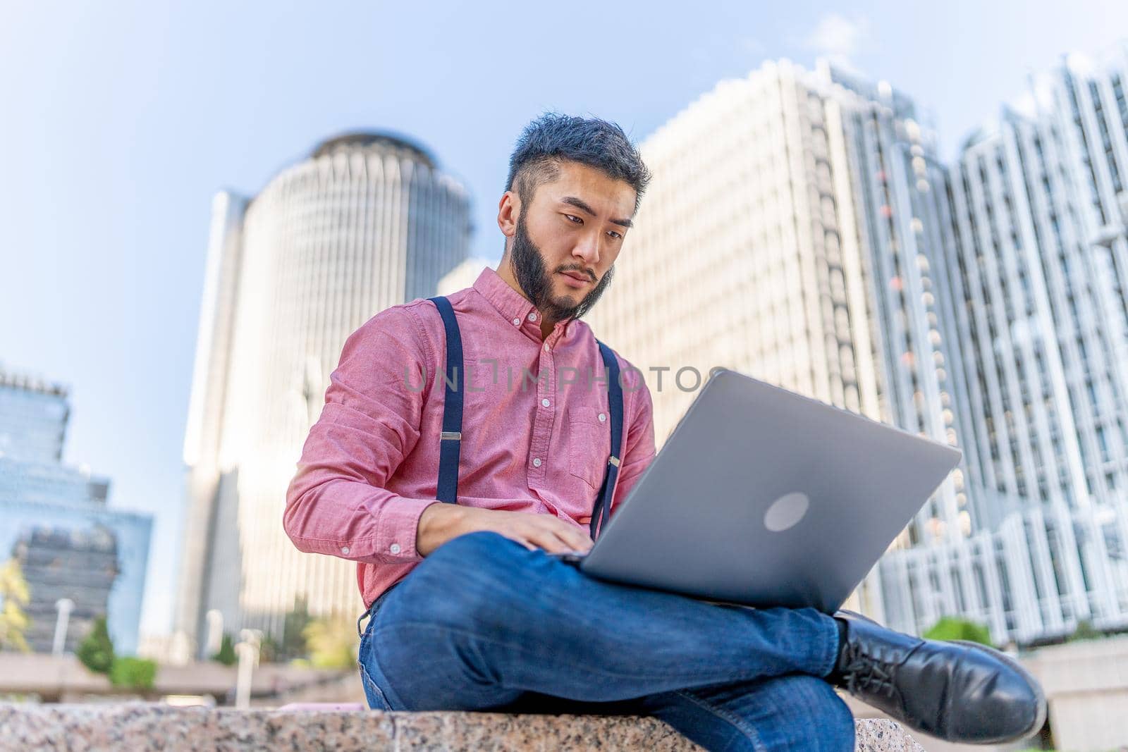 Chinese man in a shirt and braces working on a laptop in a square in a financial district