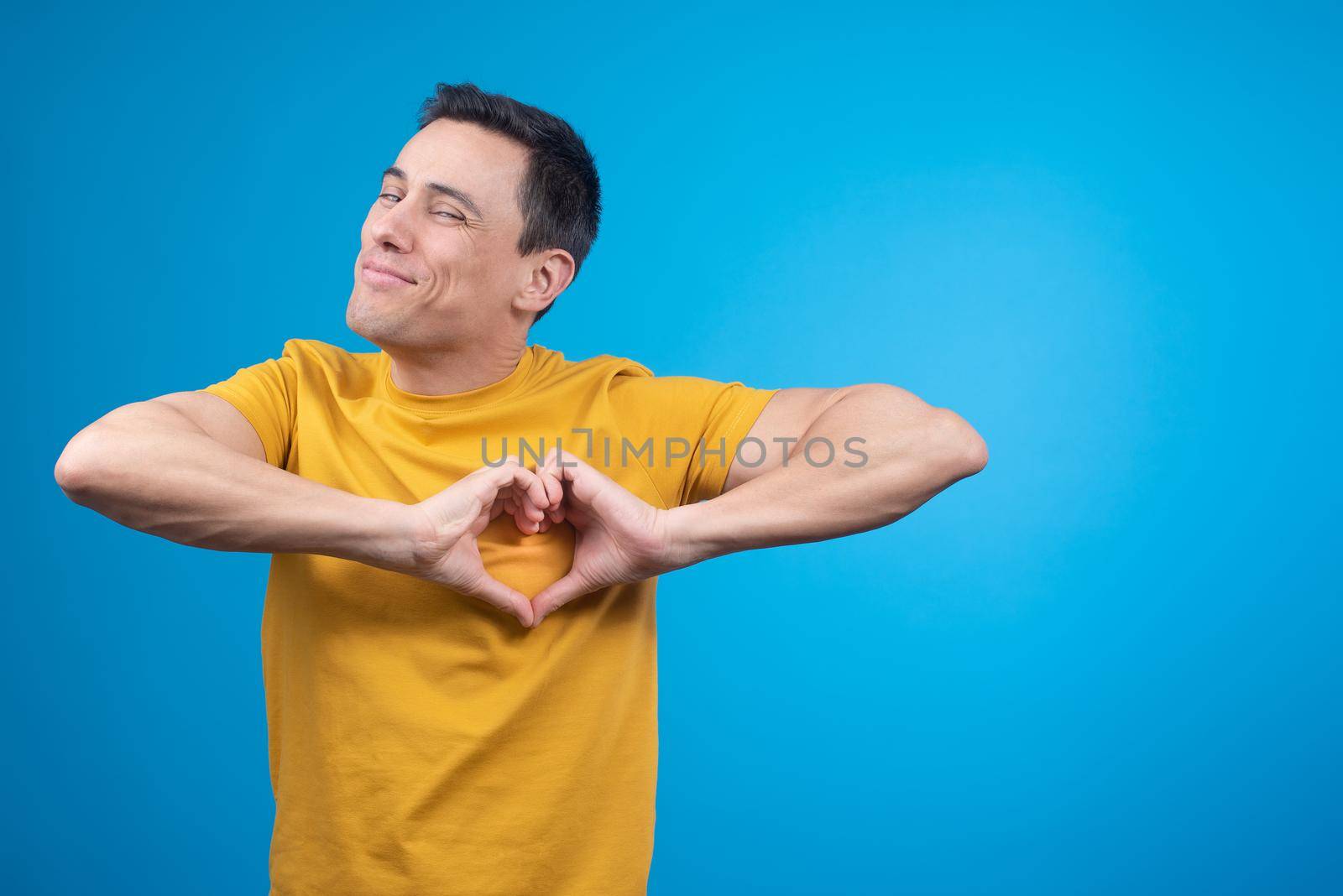 Smiling man gesturing heart on chest in blue studio by ivanmoreno