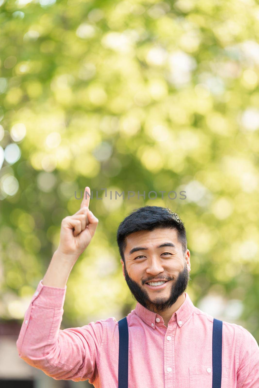 Vertical photo with copy space of an asian man in casual clothes pointing to the sky in a park