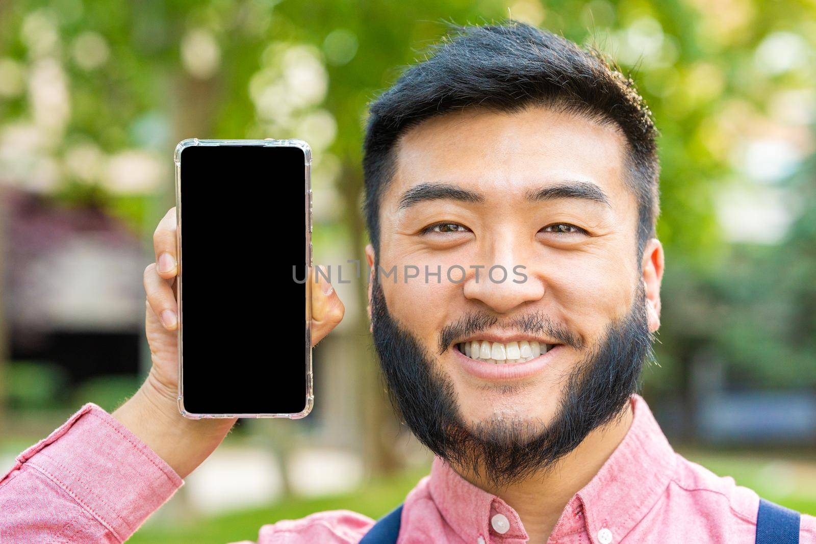 Portrait fo a happy chinese man showing the screen of a mobile phone while smiling