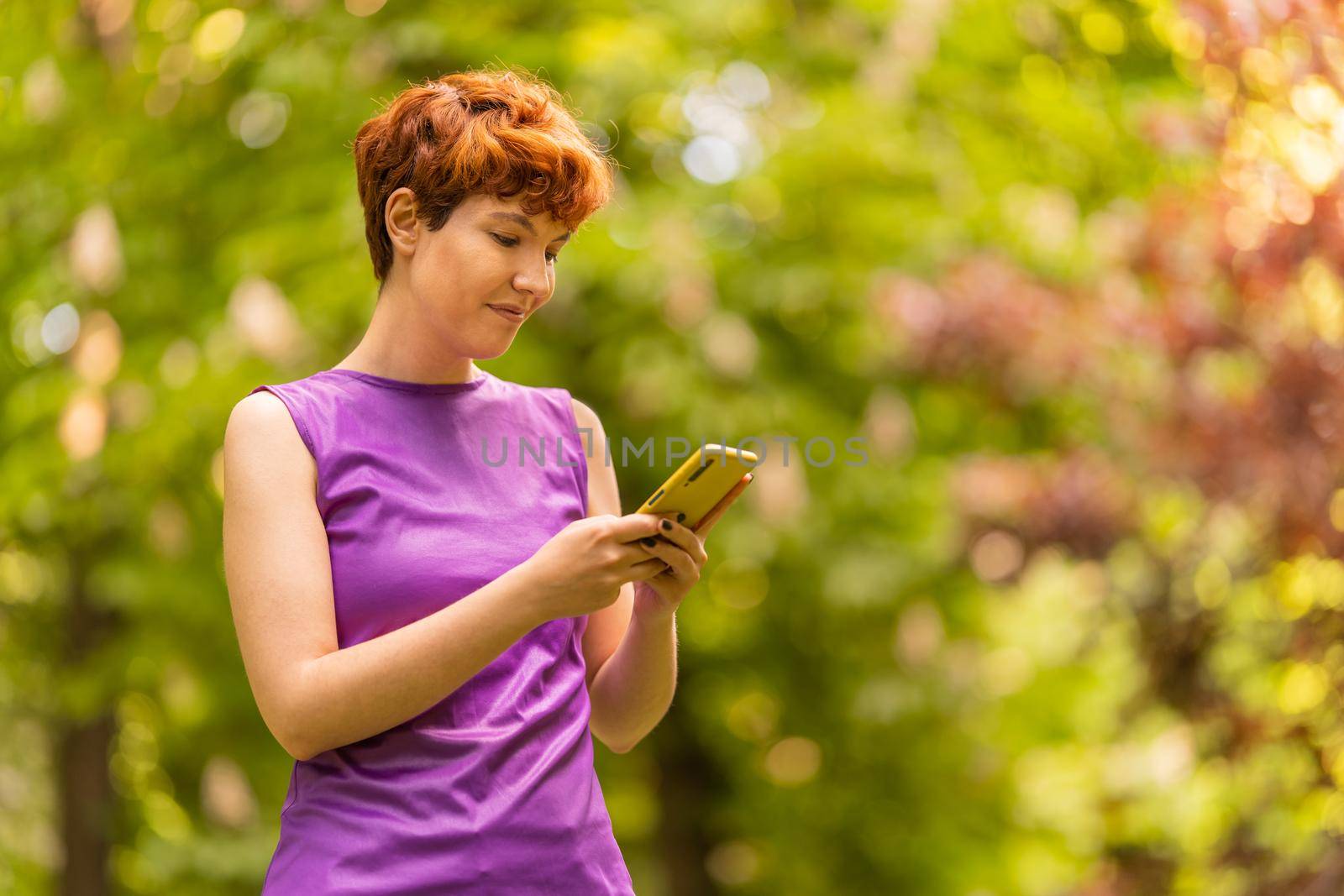 Non-binary gender person using a cellphone in the park by ivanmoreno