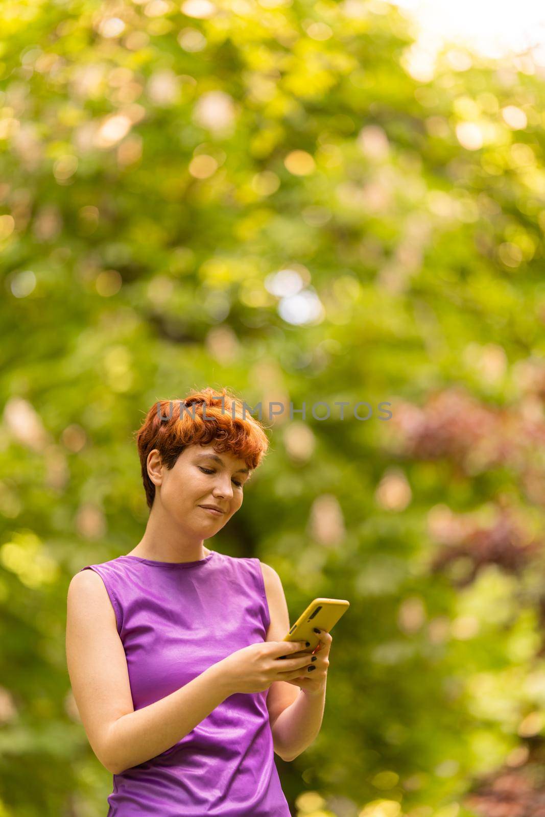 Vertical photo with copy space of a non-binary gender person using a cellphone in the park in summer