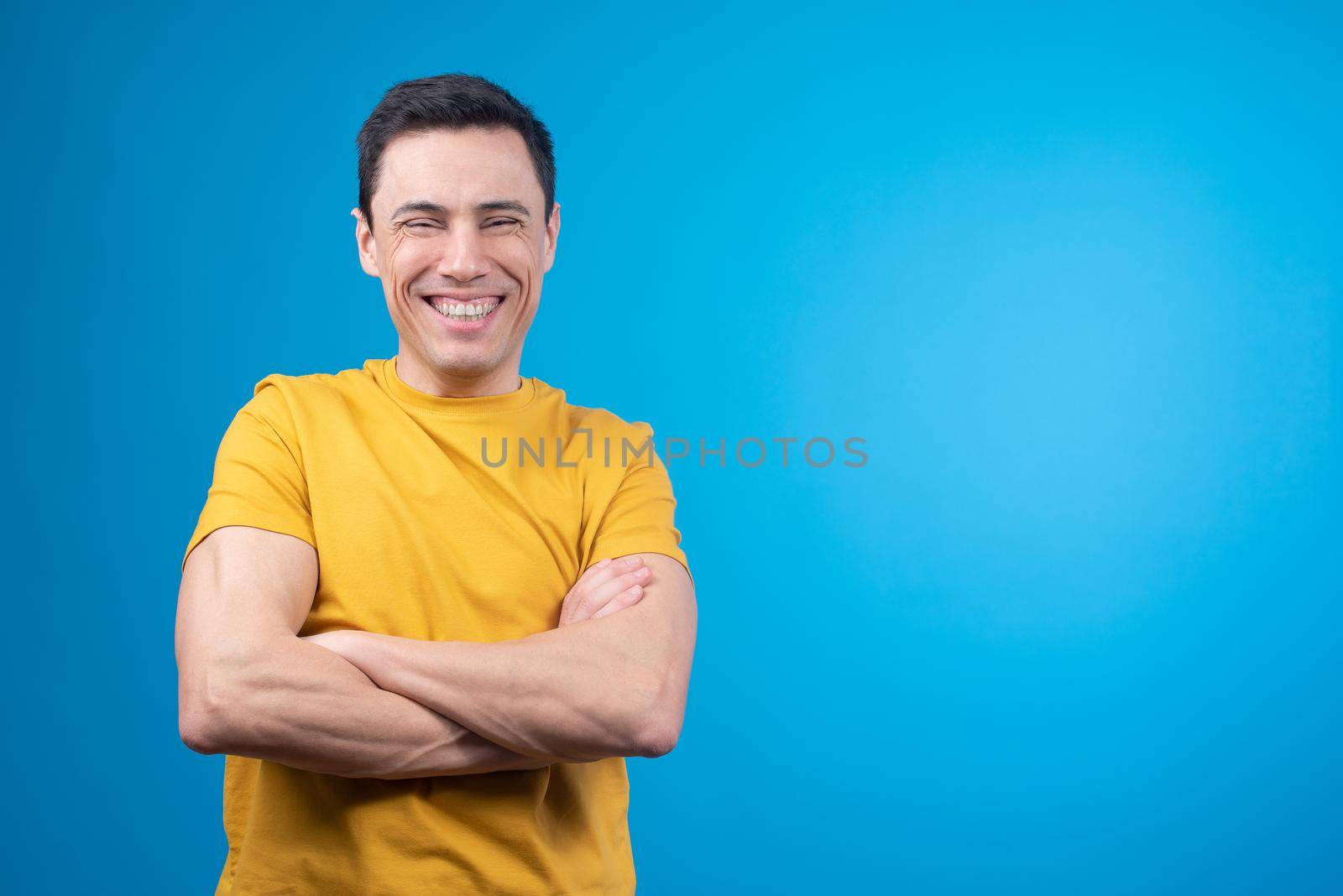 Cheerful man standing with crossed arms and laughing in studio by ivanmoreno