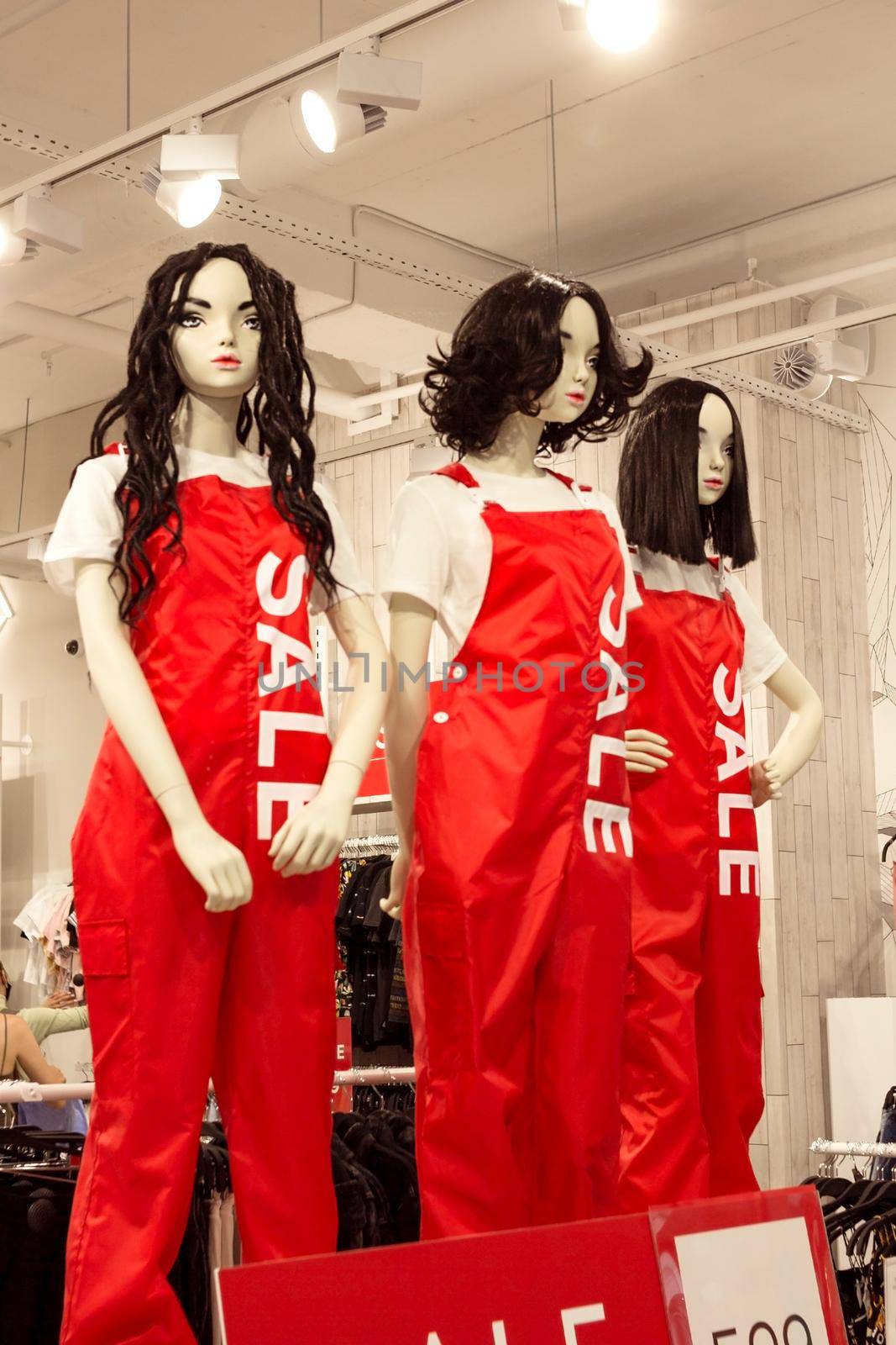 Female mannequins in woman red dungarees in fashion clothing store, black friday sale shopping concept, seasonal offer promo, vertical image