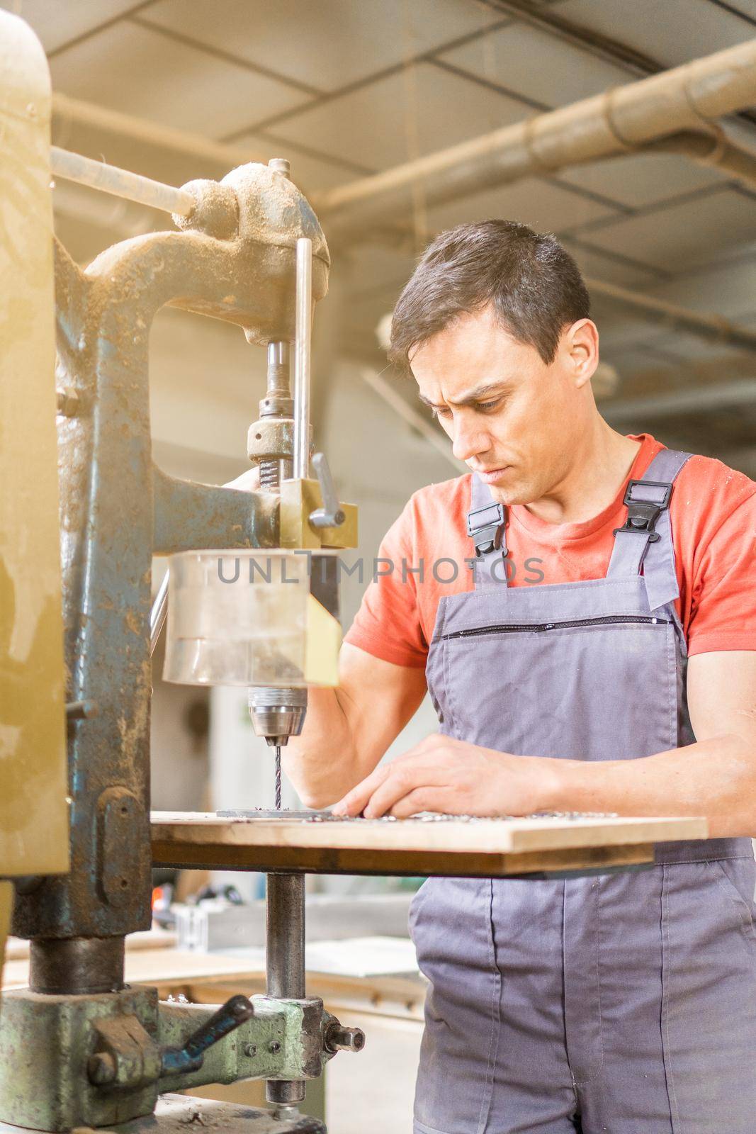 Concentrated male master in uniform drilling steel plank on professional metal machine while working in light joinery with special equipment