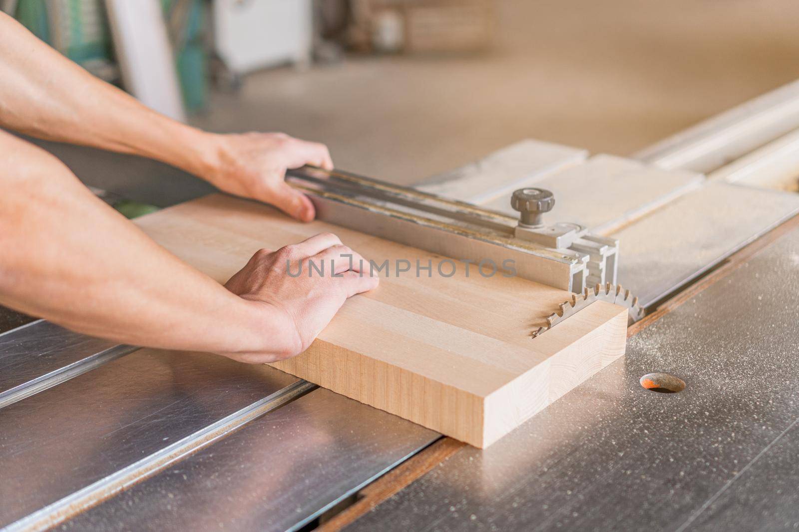 Hands of crop anonymous woodworker sawing wooden plank at squaring machine while working in light professional carpentry with special equipment