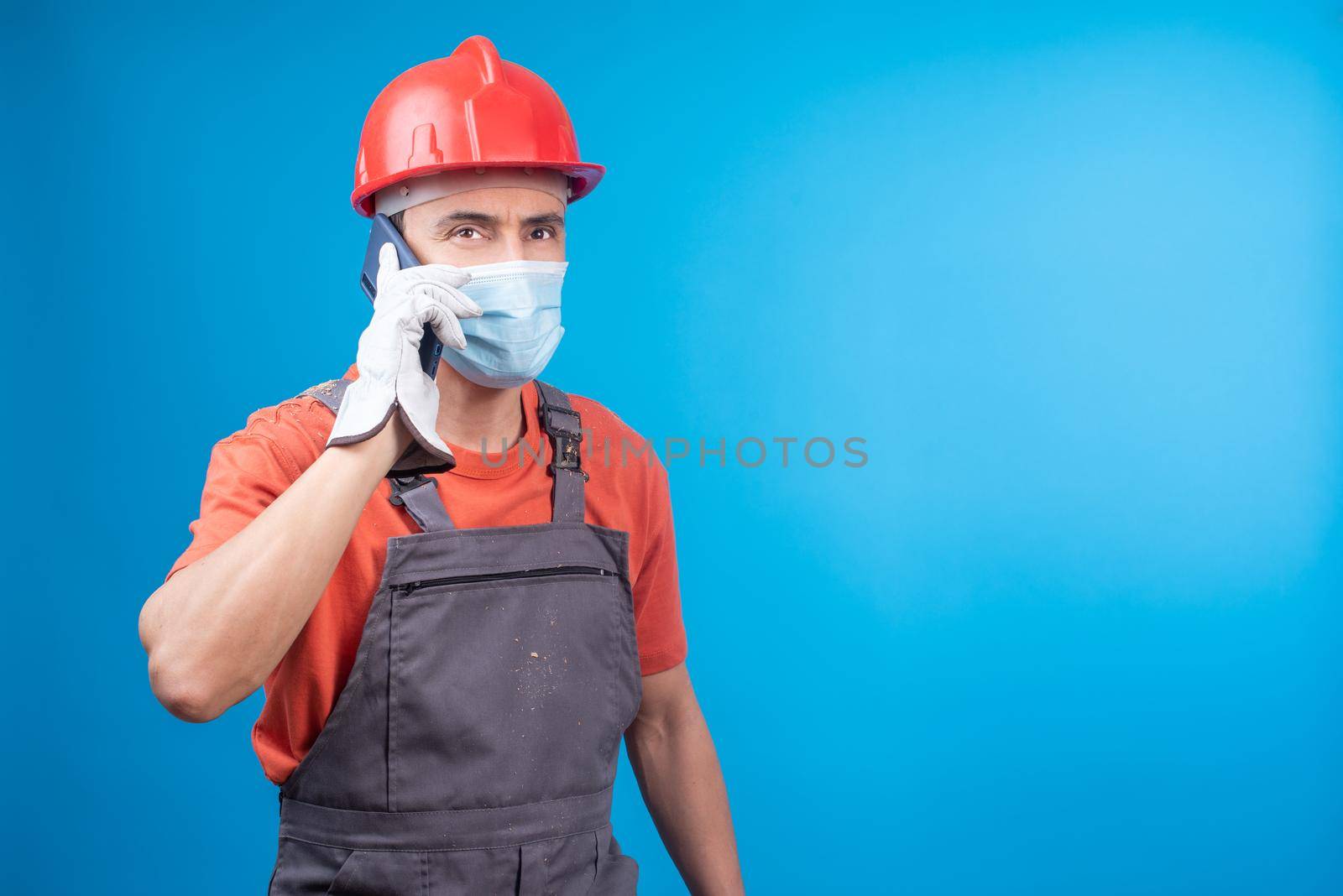 Man in builder uniform talking on smartphone during epidemic by ivanmoreno