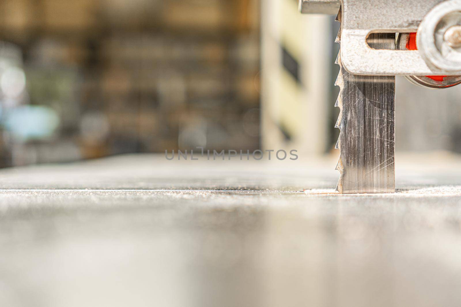 Closeup of metal band saw cutting wooden desk on blurred background of modern workshop